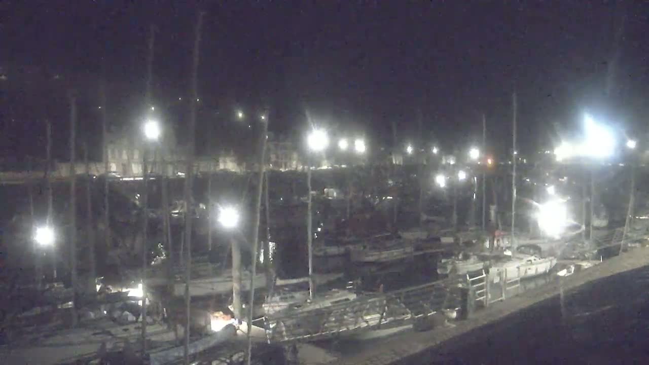 A nighttime view of a marina filled with sailboats illuminated by bright lights.
