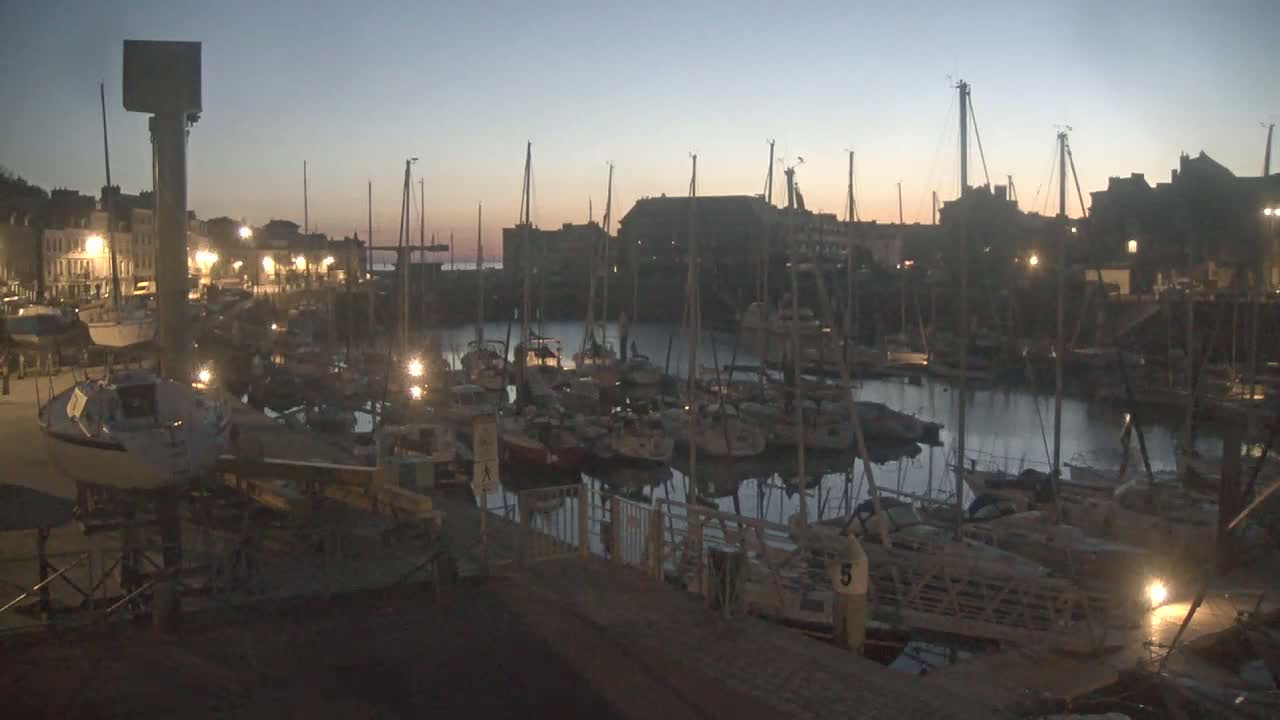 Many sailboats are moored in a harbor at twilight under a clear sky.