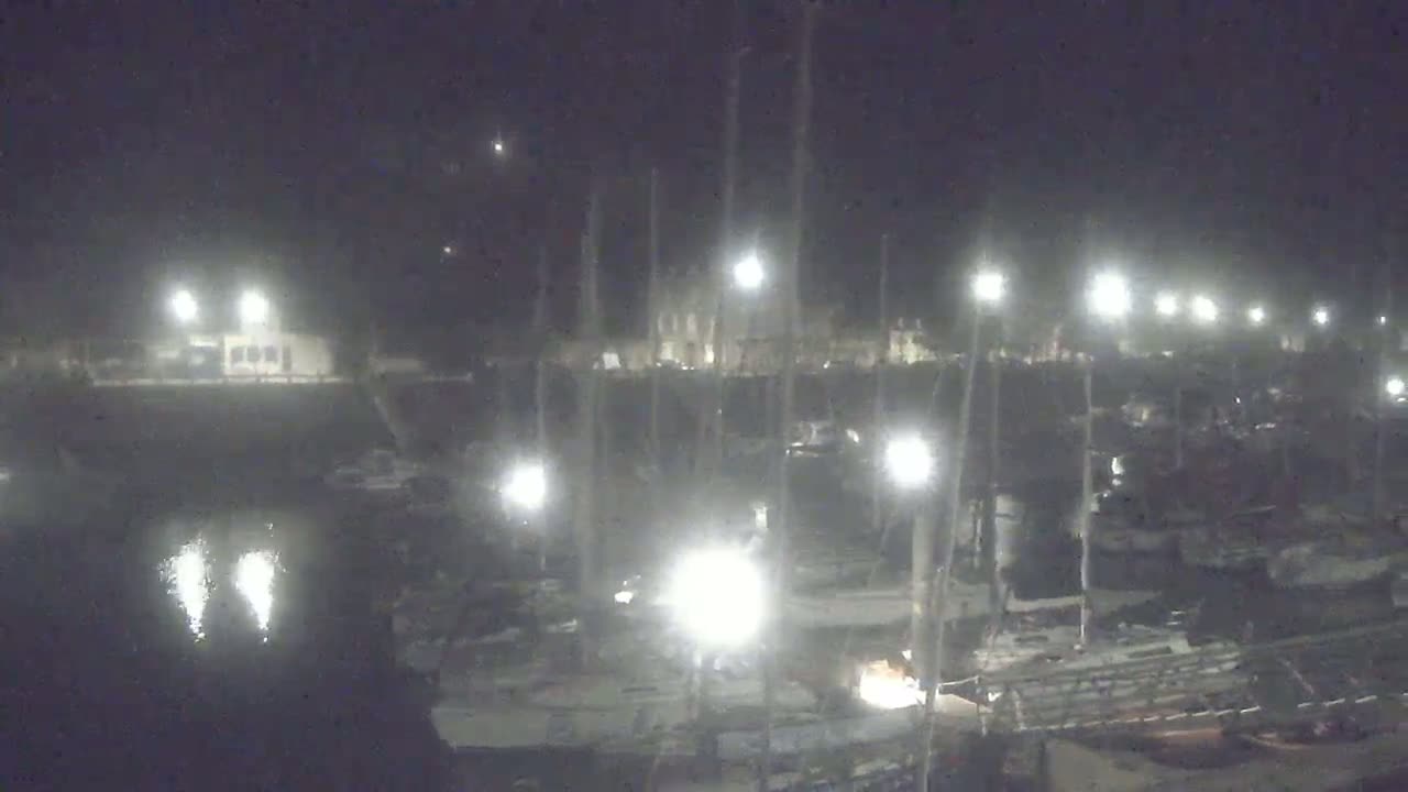 Many boats are docked at a marina at night under bright lights.