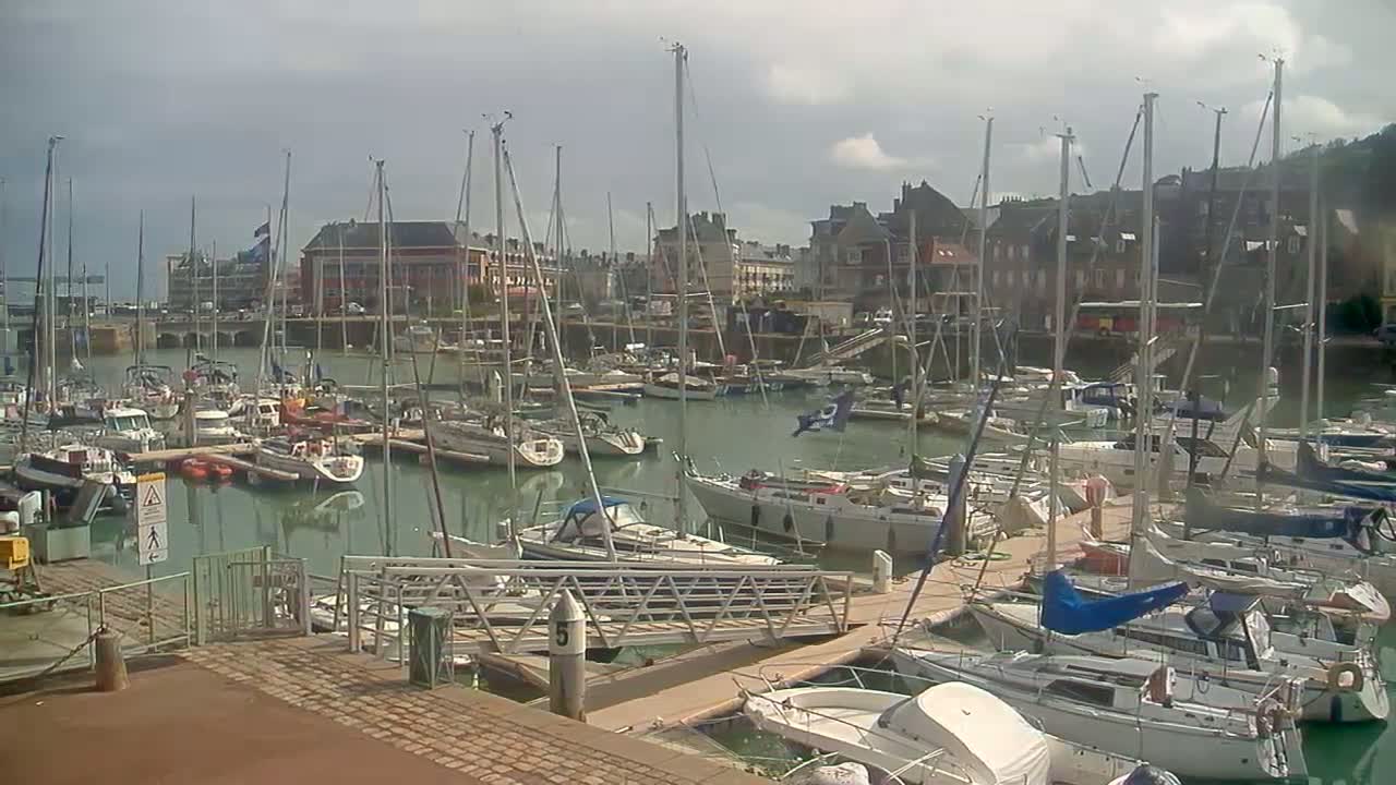 Many sailboats and motorboats are docked in a marina on a partly cloudy day.