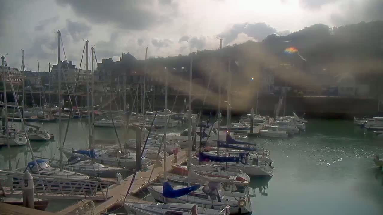 Many sailboats are docked in a harbor under a cloudy sky.