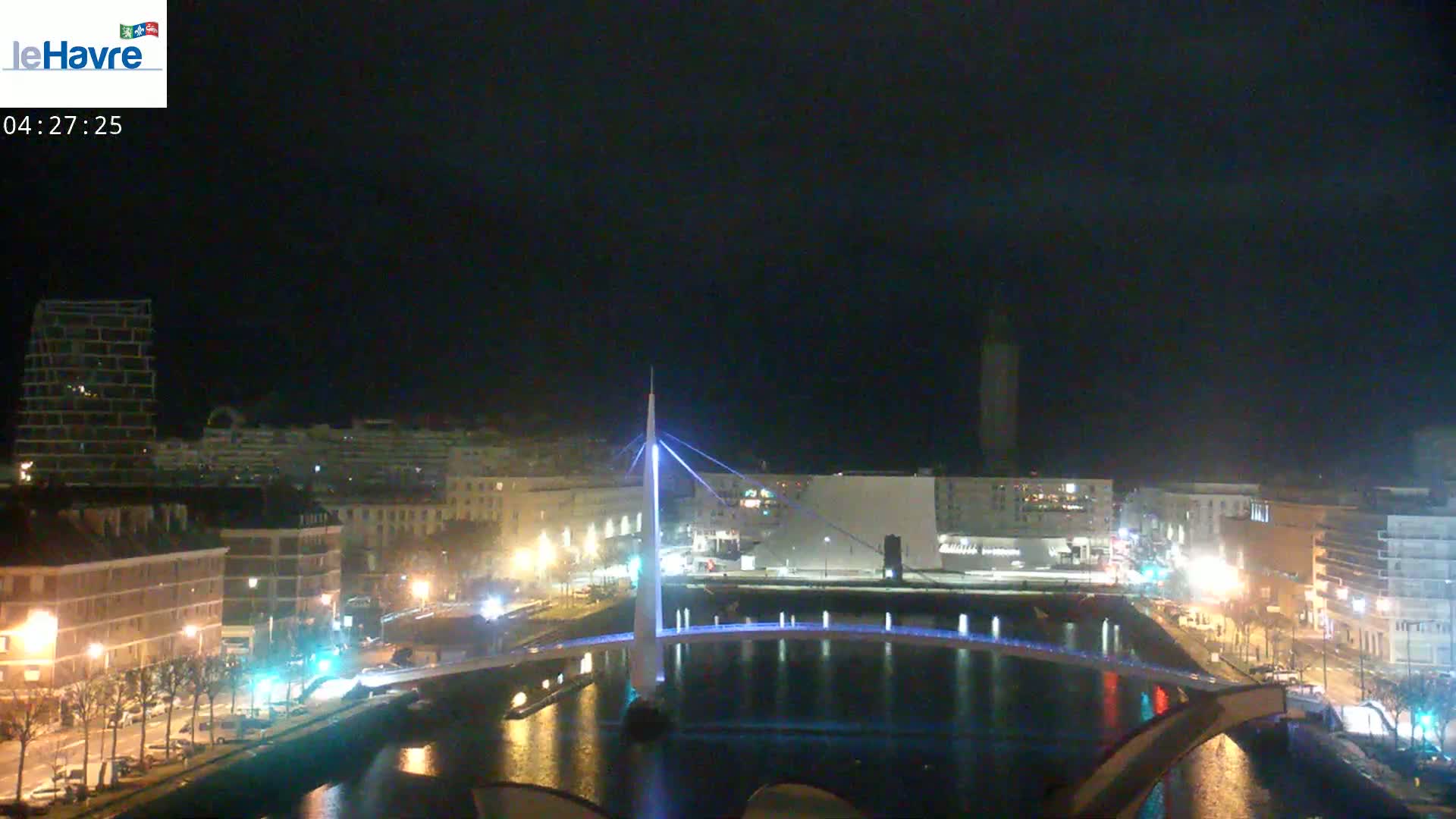 A nighttime view of a city with a lit-up bridge spanning a canal, surrounded by buildings and streetlights.