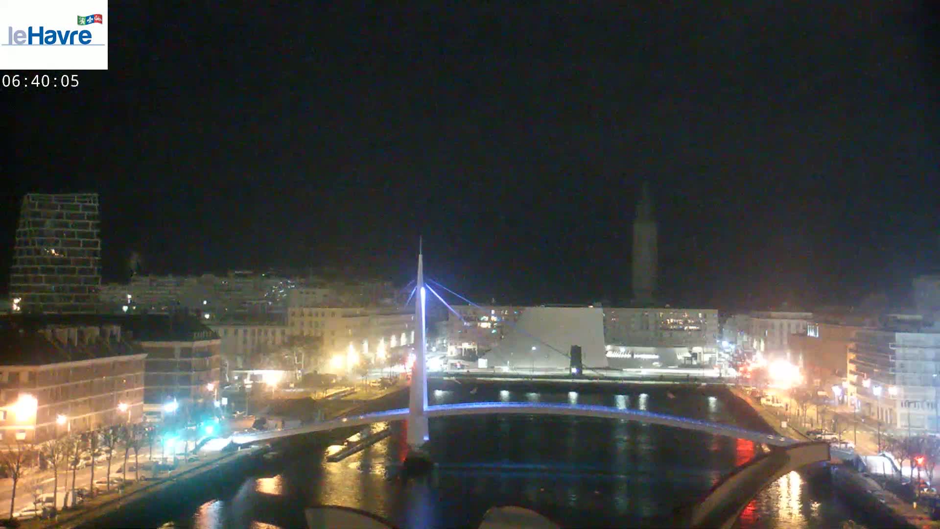 A nighttime view of a city with a lit-up bridge spanning a waterway, under a dark, clear sky.