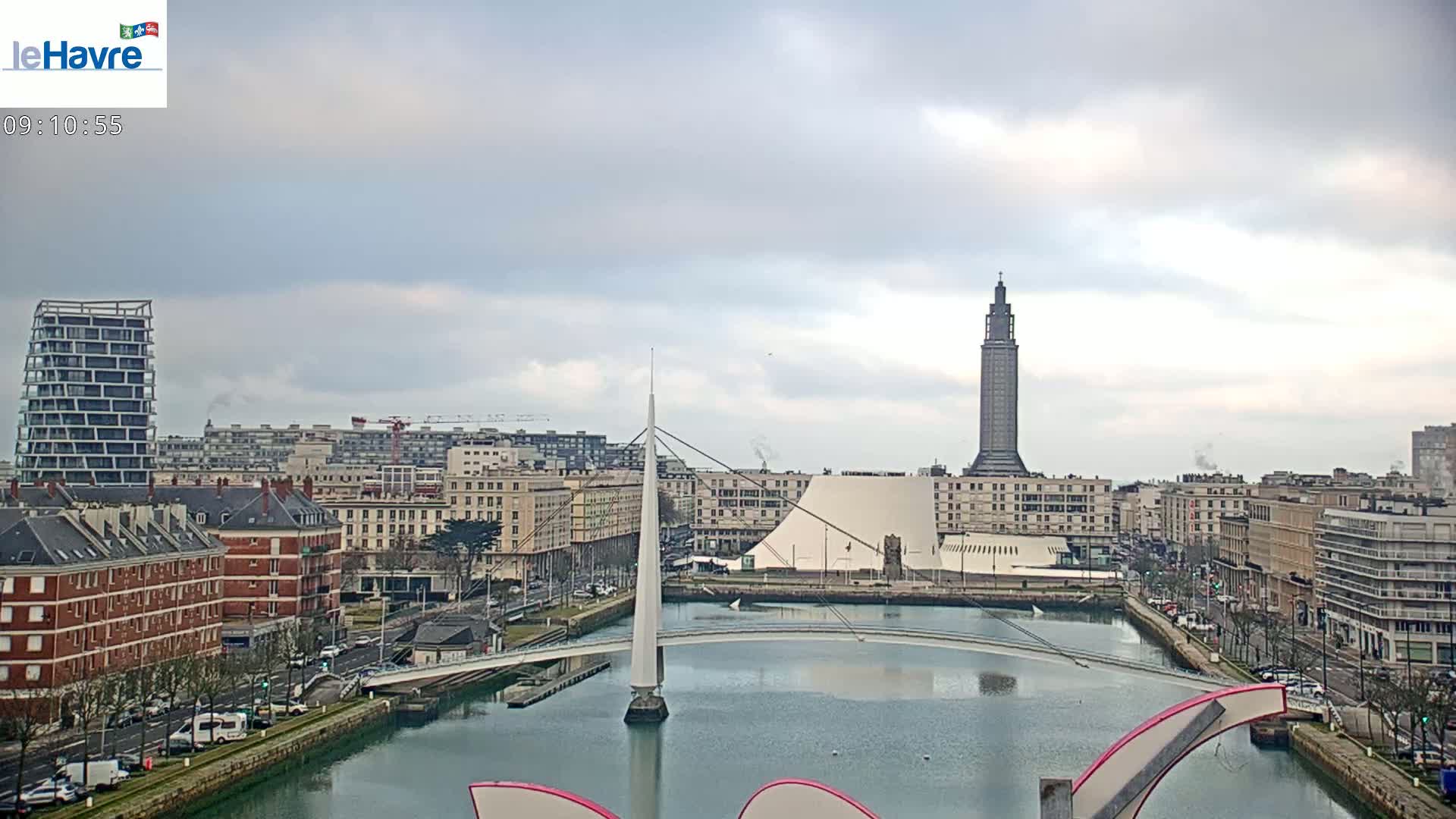 A cityscape with a canal, a modern white bridge, and a tall tower under a cloudy sky.