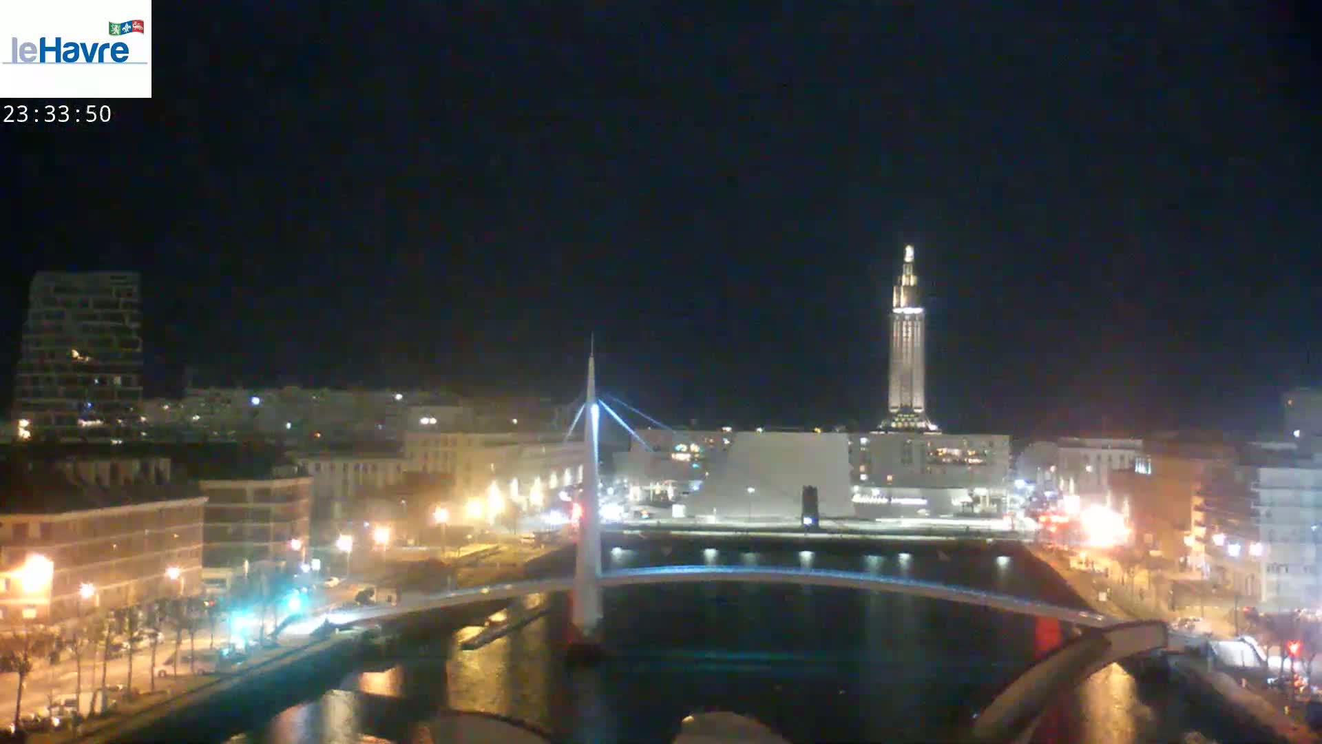A nighttime view of a city with a bridge and a tall tower illuminated against a dark sky.