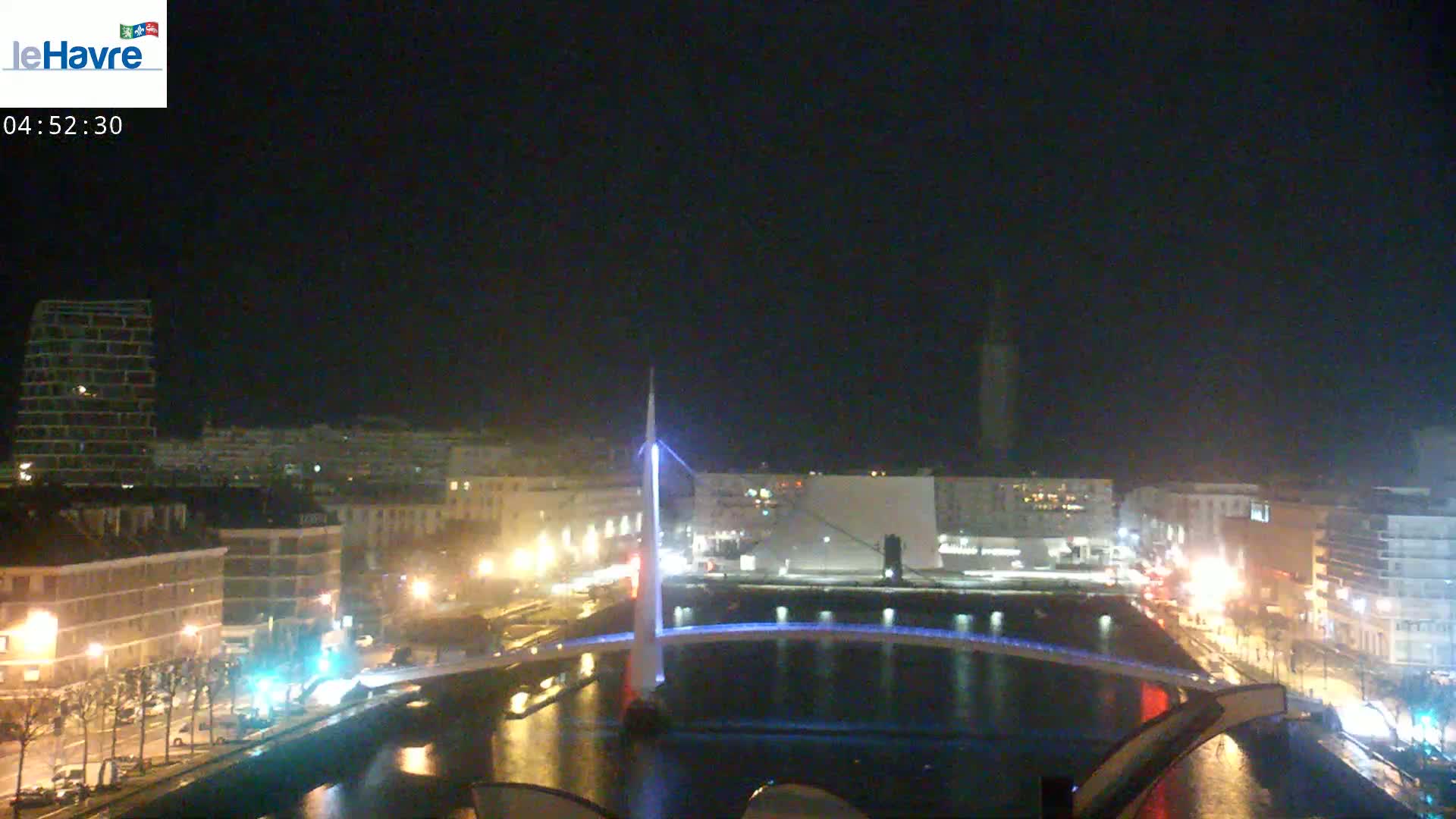 A nighttime view of a city with a lit bridge spanning a dark waterway, under a clear, dark sky.