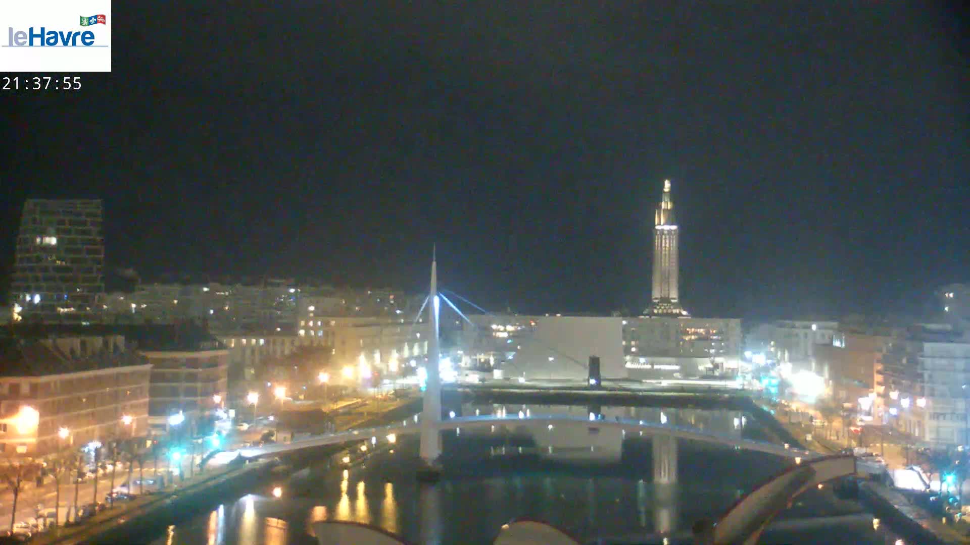 A nighttime view of a city with a tall tower and a bridge spanning a waterway, under a clear dark sky.