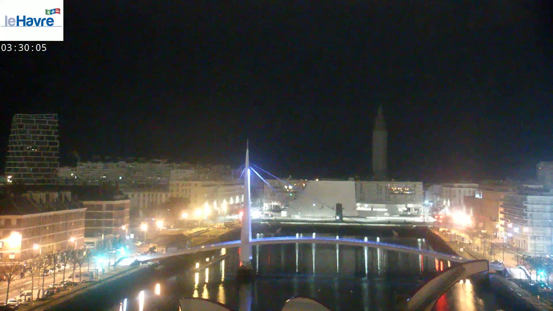 A nighttime view of a city with a lit-up bridge spanning a waterway, under a clear, dark sky.