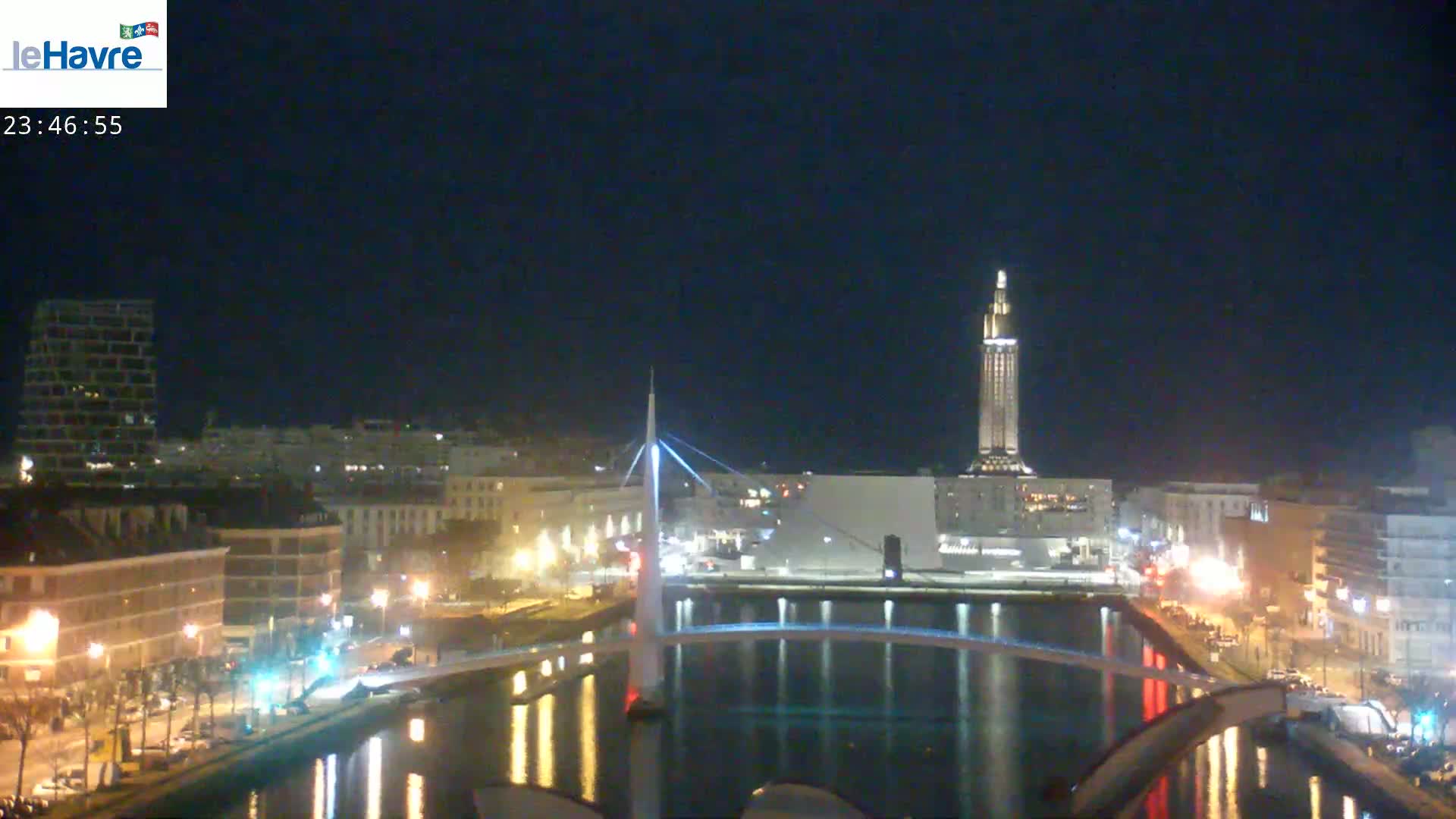 A nighttime view of a city waterfront, showing a bridge, buildings, and a tall tower, under a clear, dark sky.