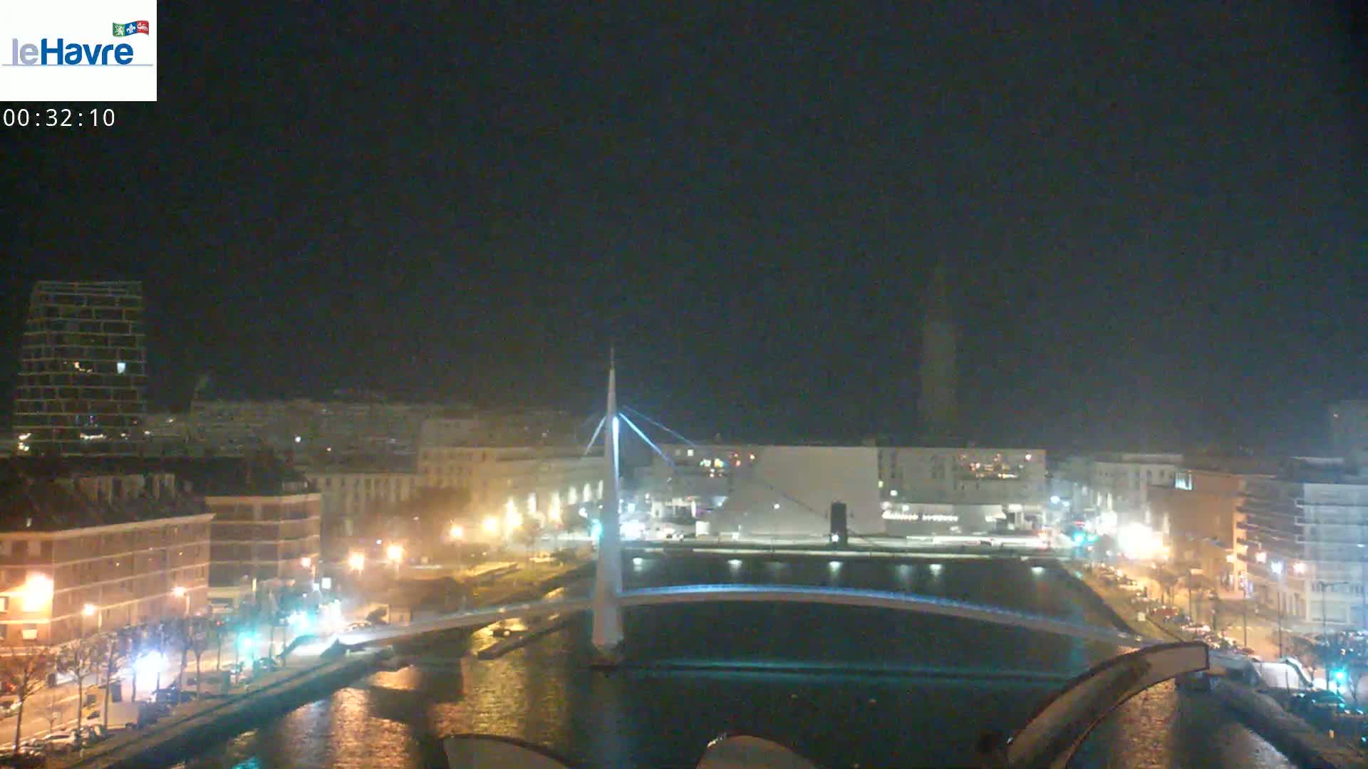A nighttime view of a city with a lit-up bridge spanning a waterway, under a clear, dark sky.