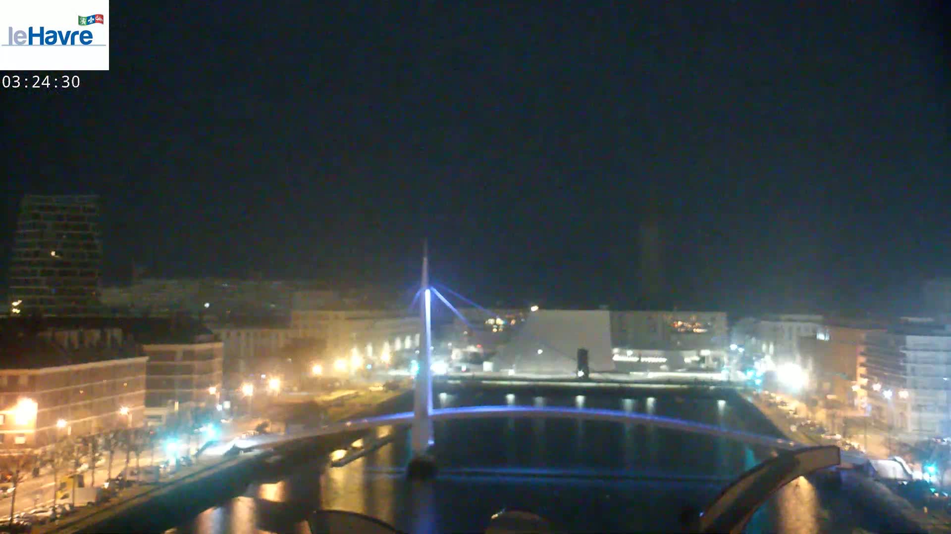 A nighttime view of a city with a lit-up bridge spanning a waterway, under a clear, dark sky.