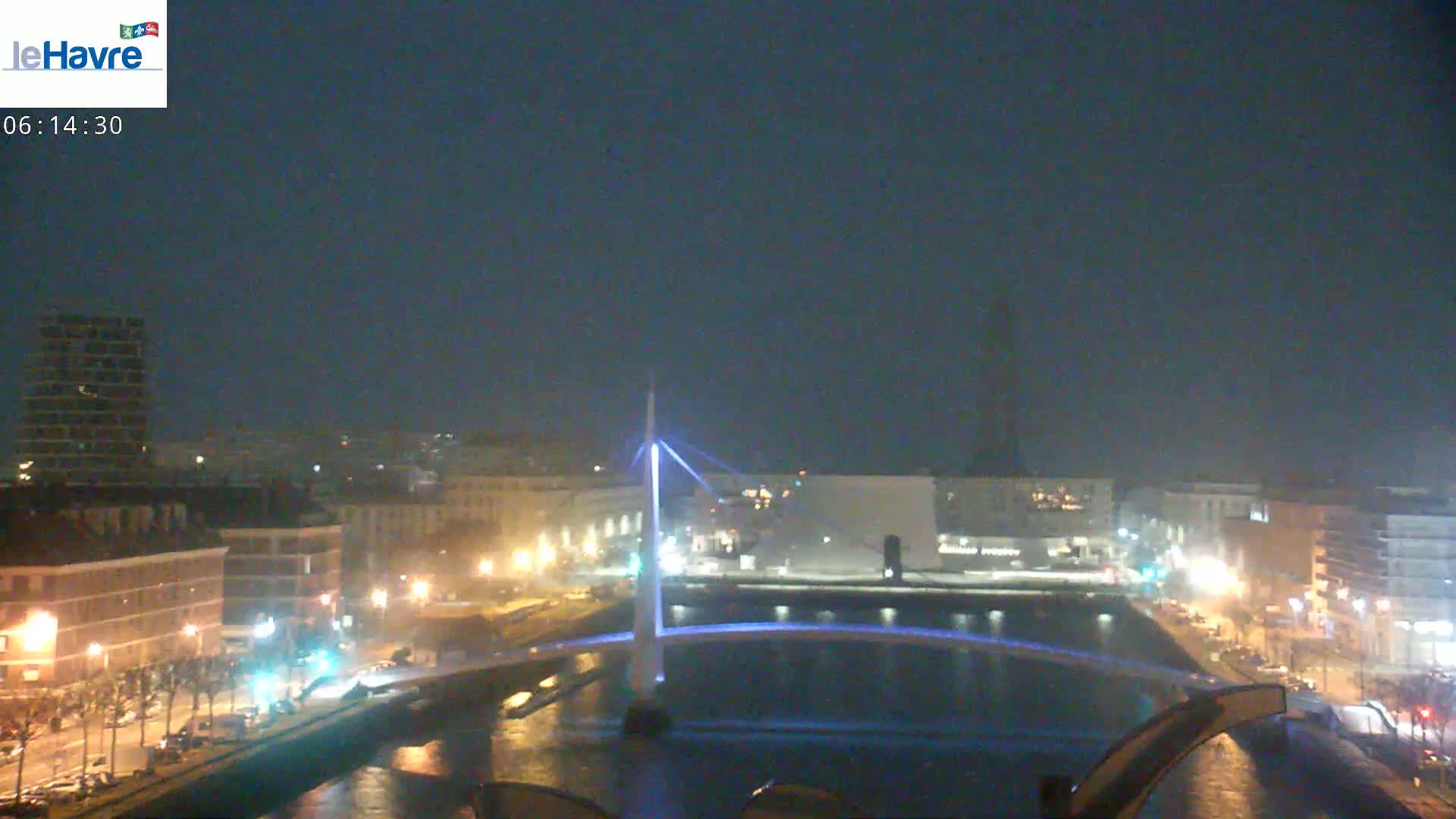 A nighttime view of a city with a lit-up bridge spanning a waterway, under a dark, clear sky.