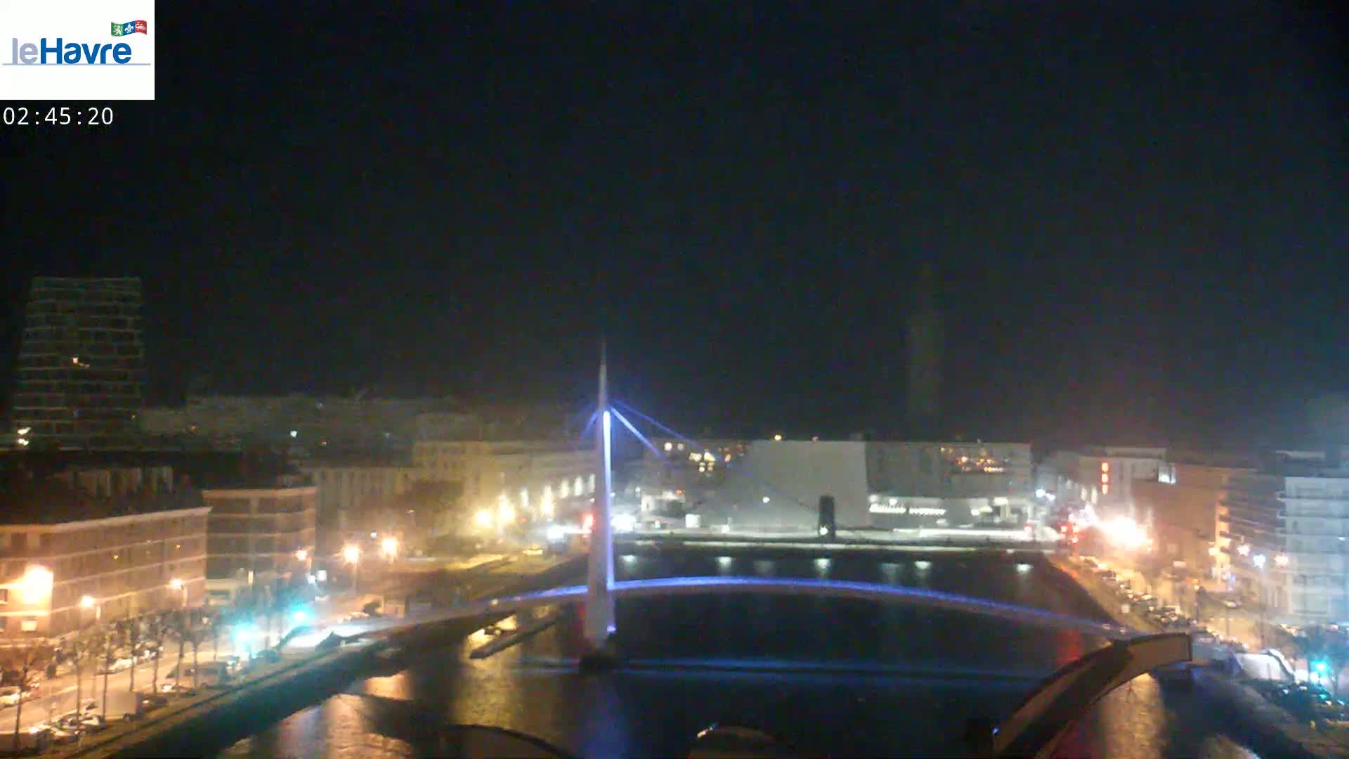 A nighttime view of a city with a lit-up bridge spanning a waterway, under a dark, clear sky.