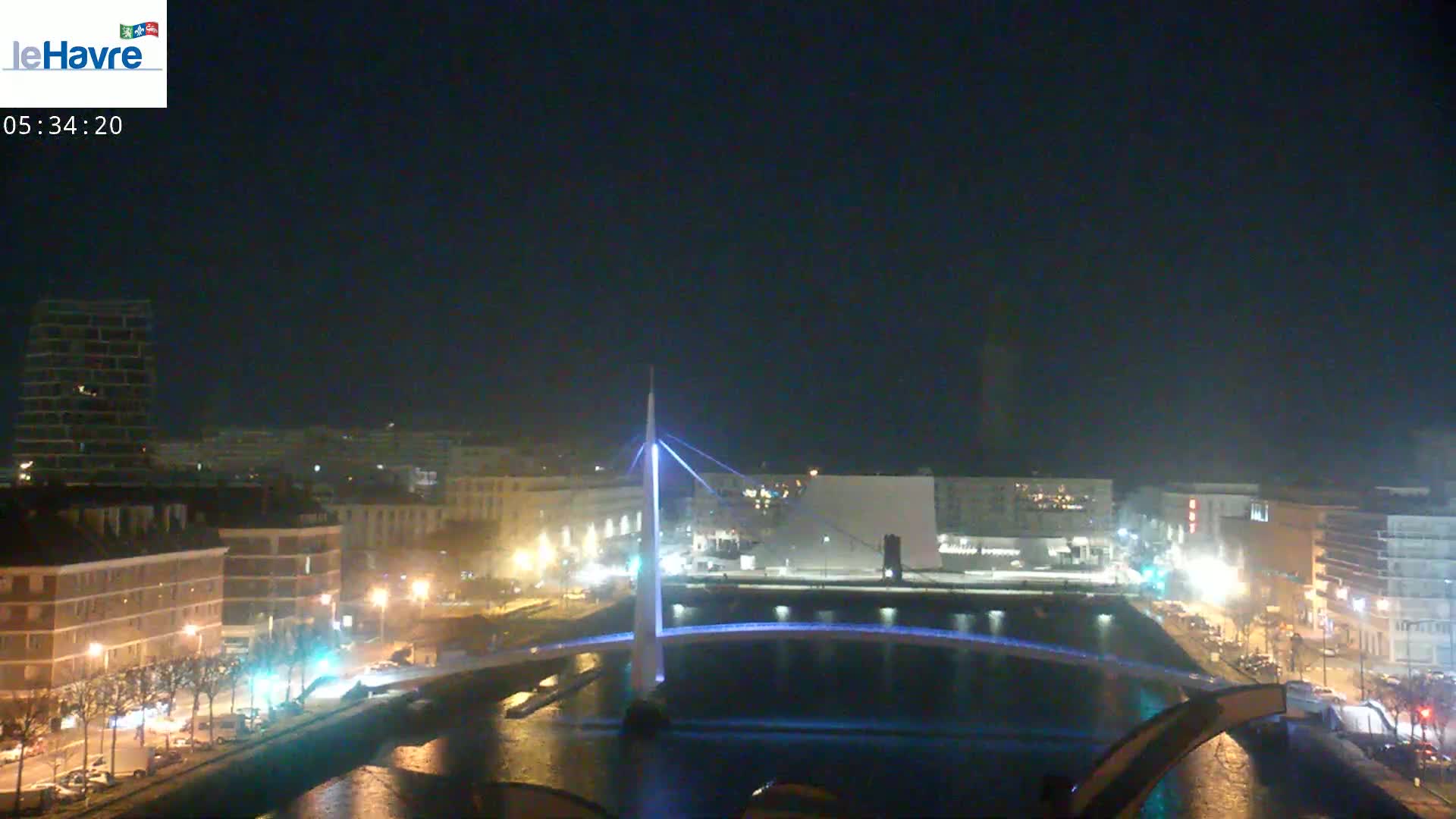 A nighttime view of a city with a lit-up bridge spanning a waterway, under a clear, dark sky.