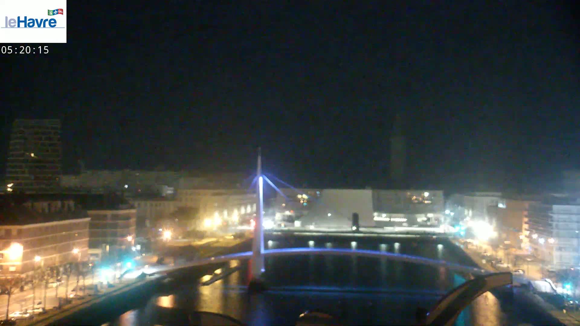 A nighttime view of a city canal with a lit bridge and buildings along the waterfront under a clear, dark sky.