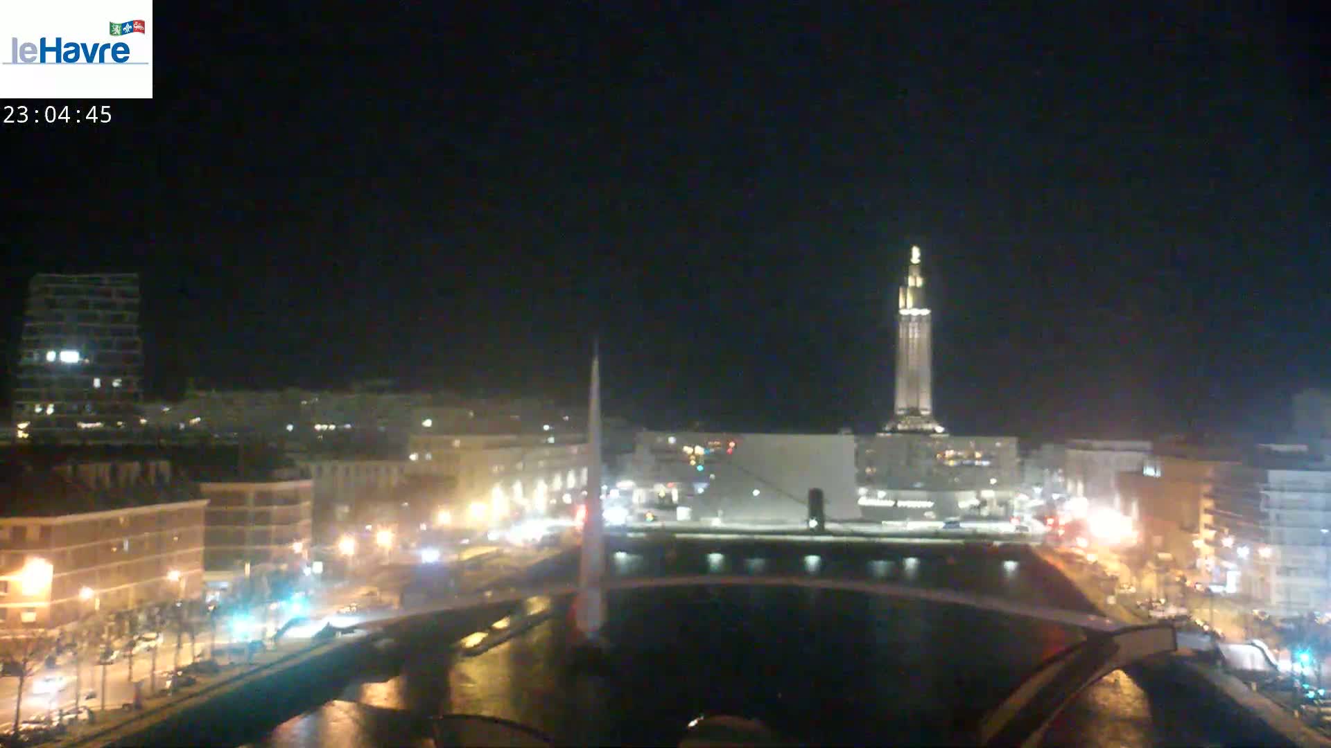 A nighttime view of a city with a tall illuminated tower, a river, and bridges, under a clear sky.