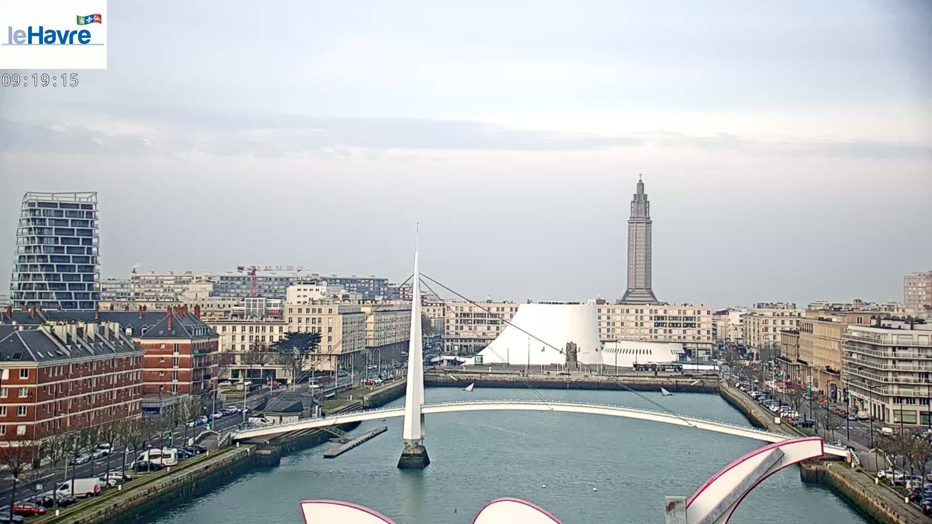 A city skyline with a white bridge spanning a waterway, under a cloudy sky.