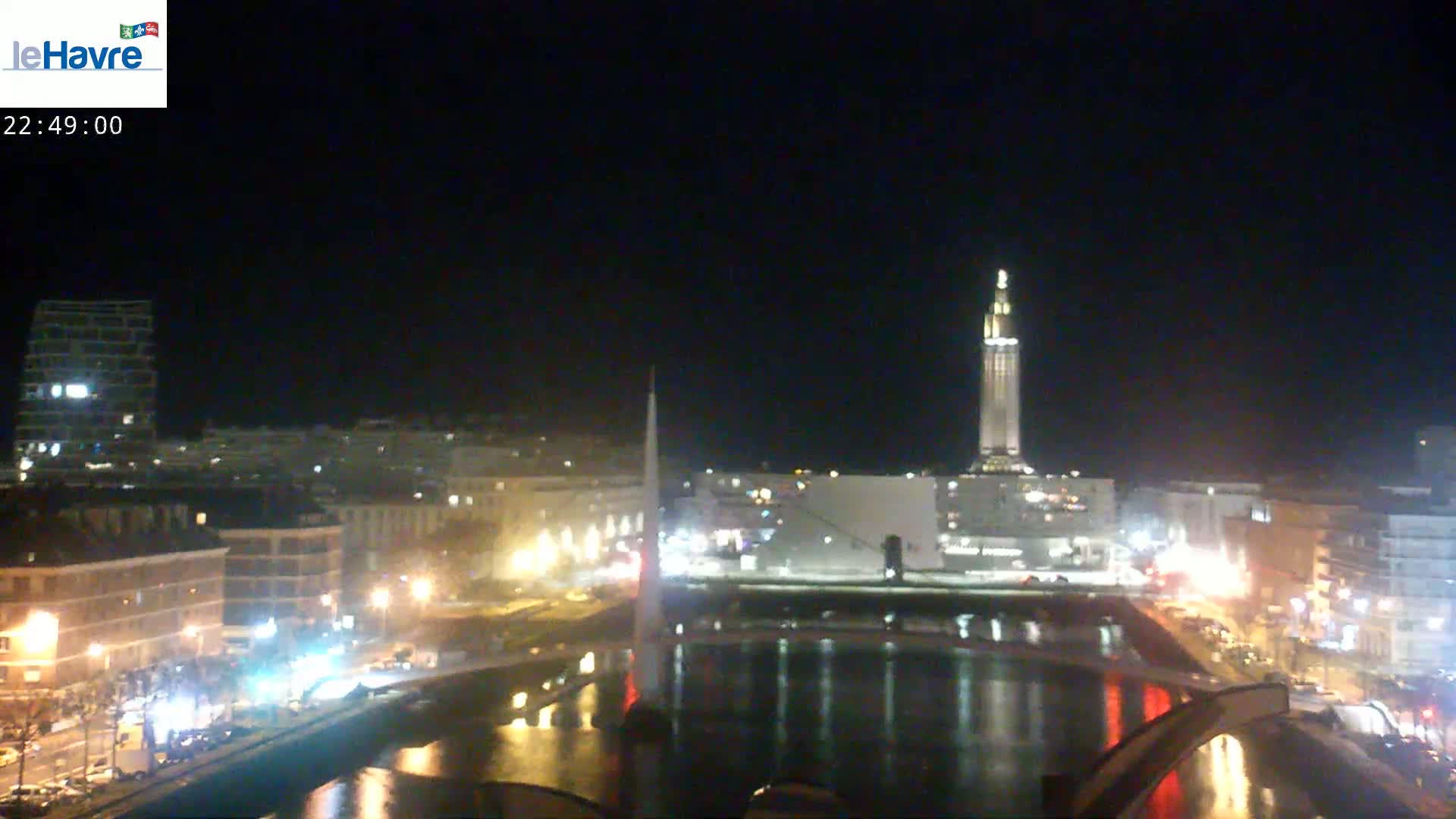 A nighttime cityscape with a tall tower and a body of water reflecting city lights.