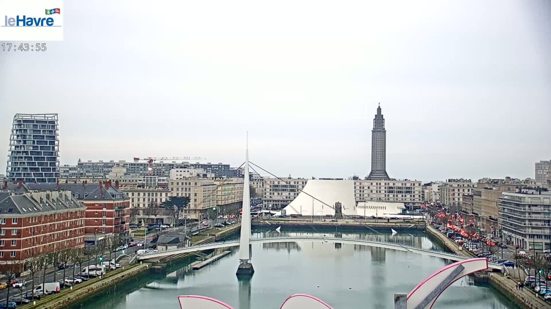 A cityscape with a canal, a modern bridge, and a tall tower under an overcast sky.