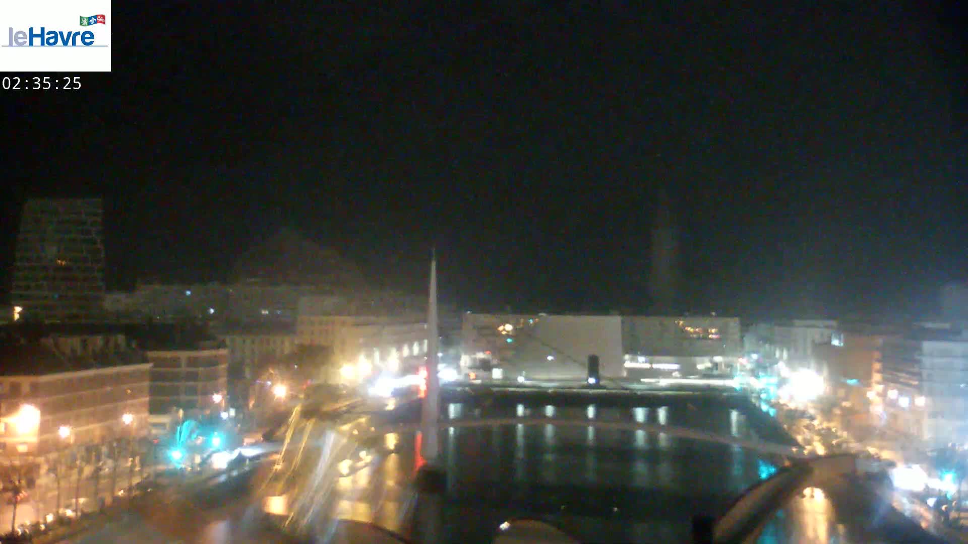 A nighttime view of a city harbor with calm water reflecting city lights under a dark, clear sky.