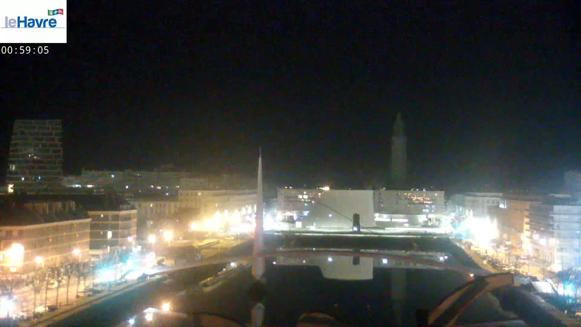 A nighttime view of a city with illuminated buildings and streets, a tall structure in the distance, and a dark sky.