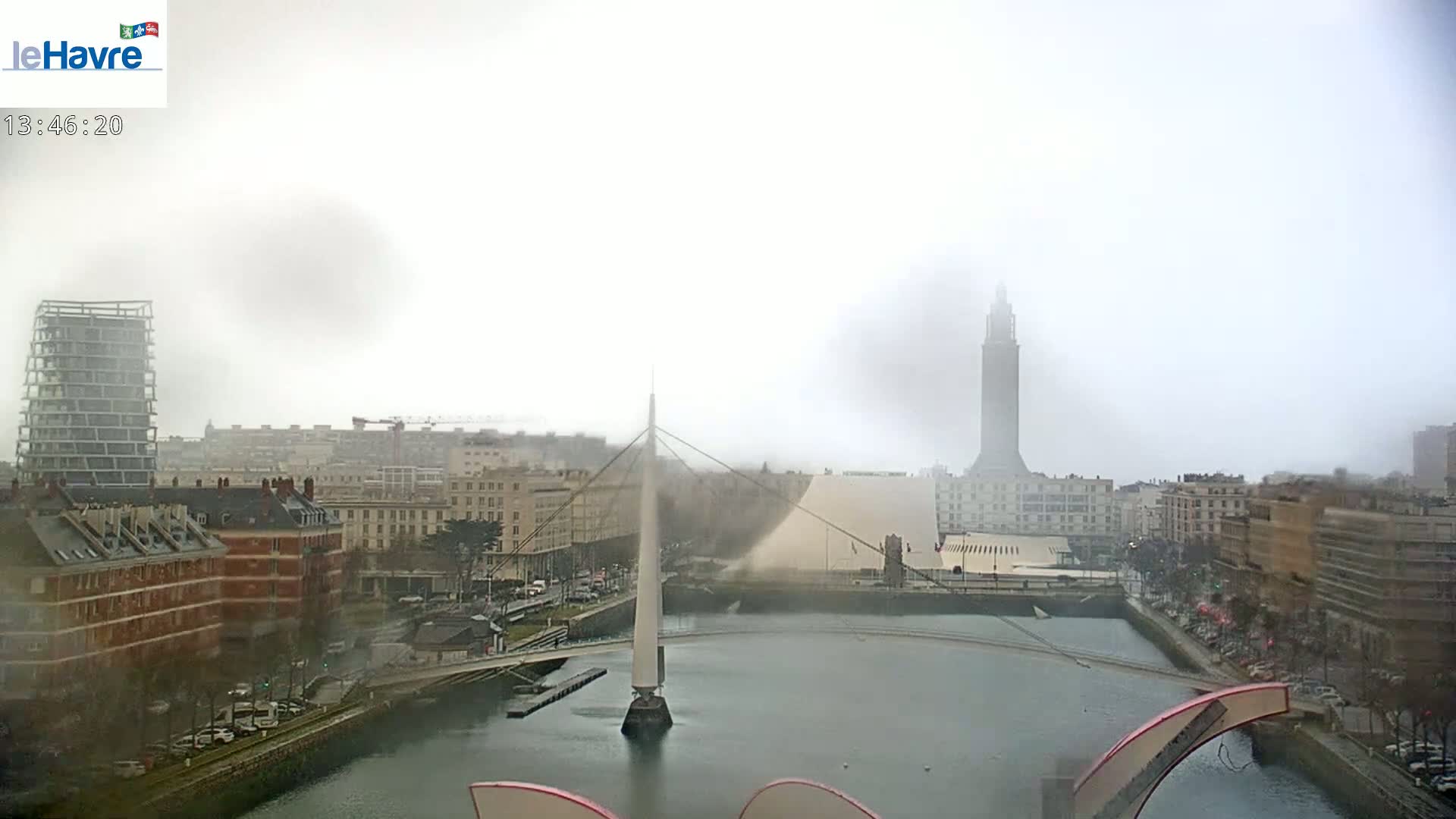 A foggy city scene shows a canal with a bridge and several buildings, including a tall tower.