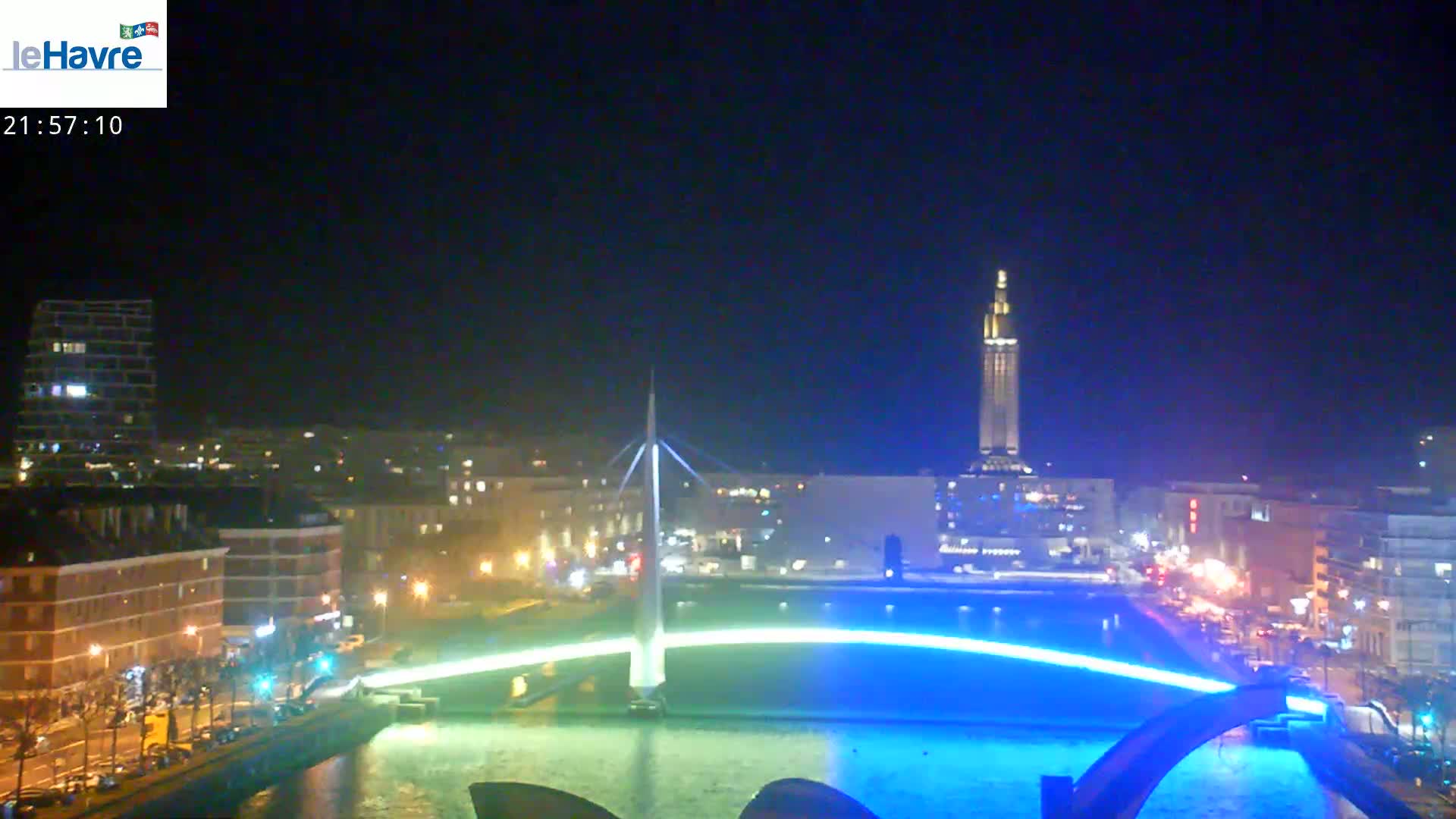 A nighttime view of a city with a lit-up bridge spanning a waterway, under a clear dark sky.