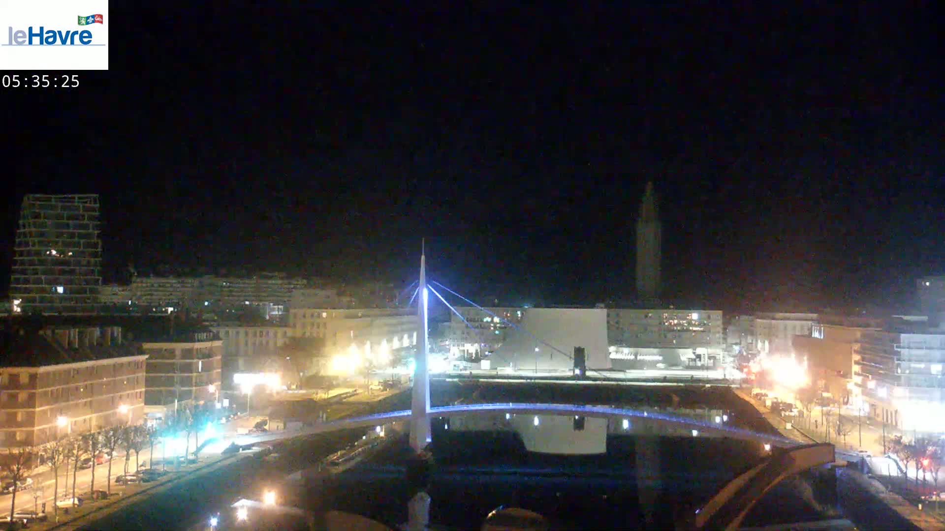A nighttime view of a city with a illuminated bridge over a canal, buildings, and streetlights.