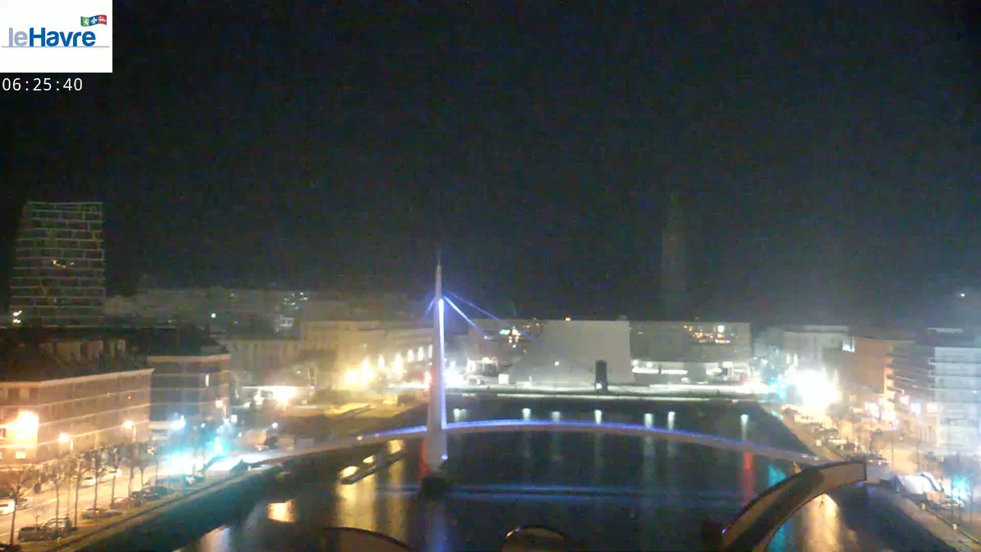 A nighttime view of a city with a lit-up bridge spanning a canal, under a clear, dark sky.