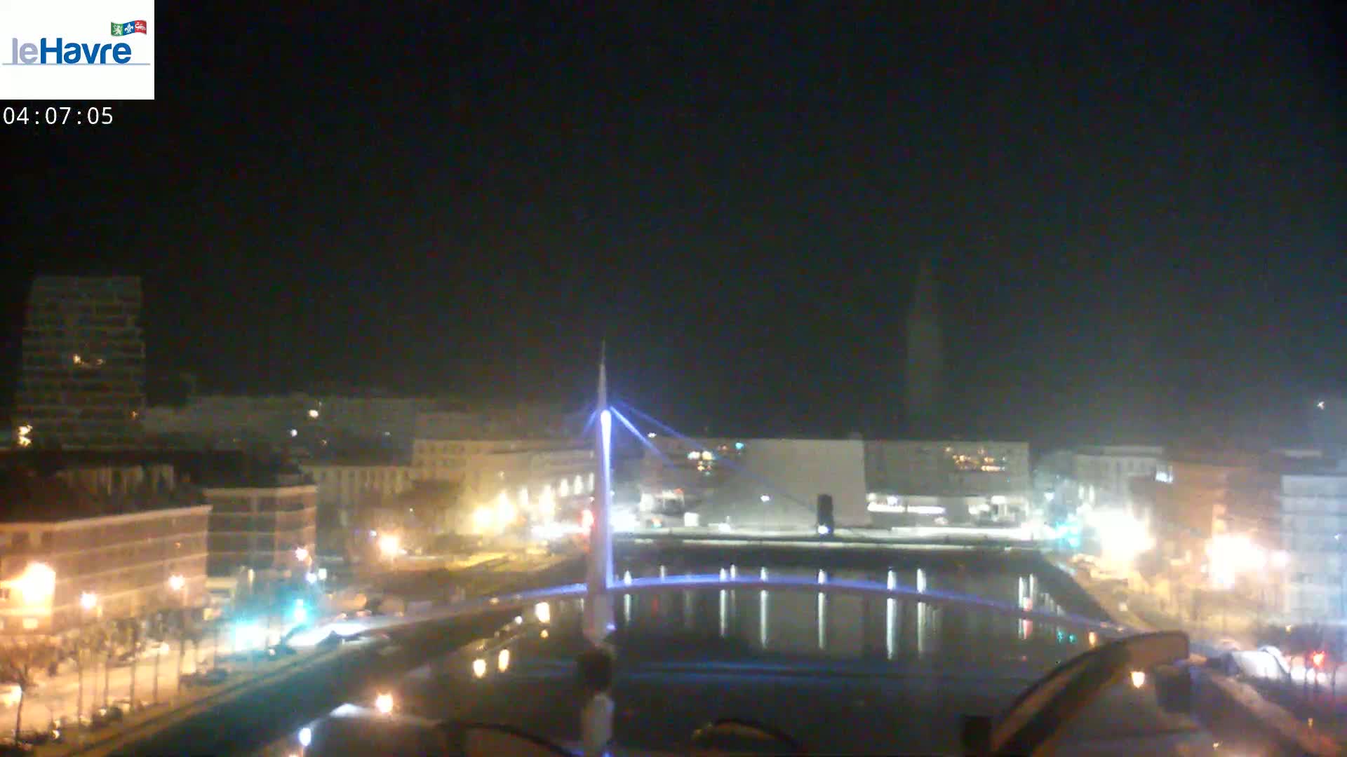 A nighttime view of a city with a lit-up bridge spanning a canal, under a clear, dark sky.