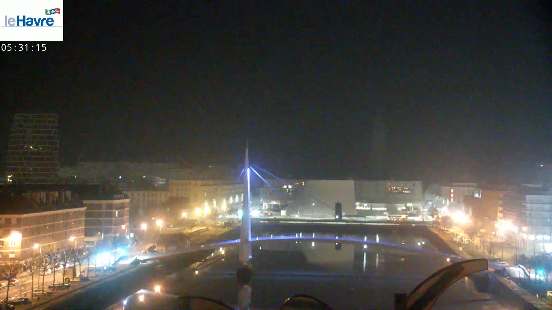 A nighttime view of a city with a lit bridge spanning a body of water, under a clear, dark sky.