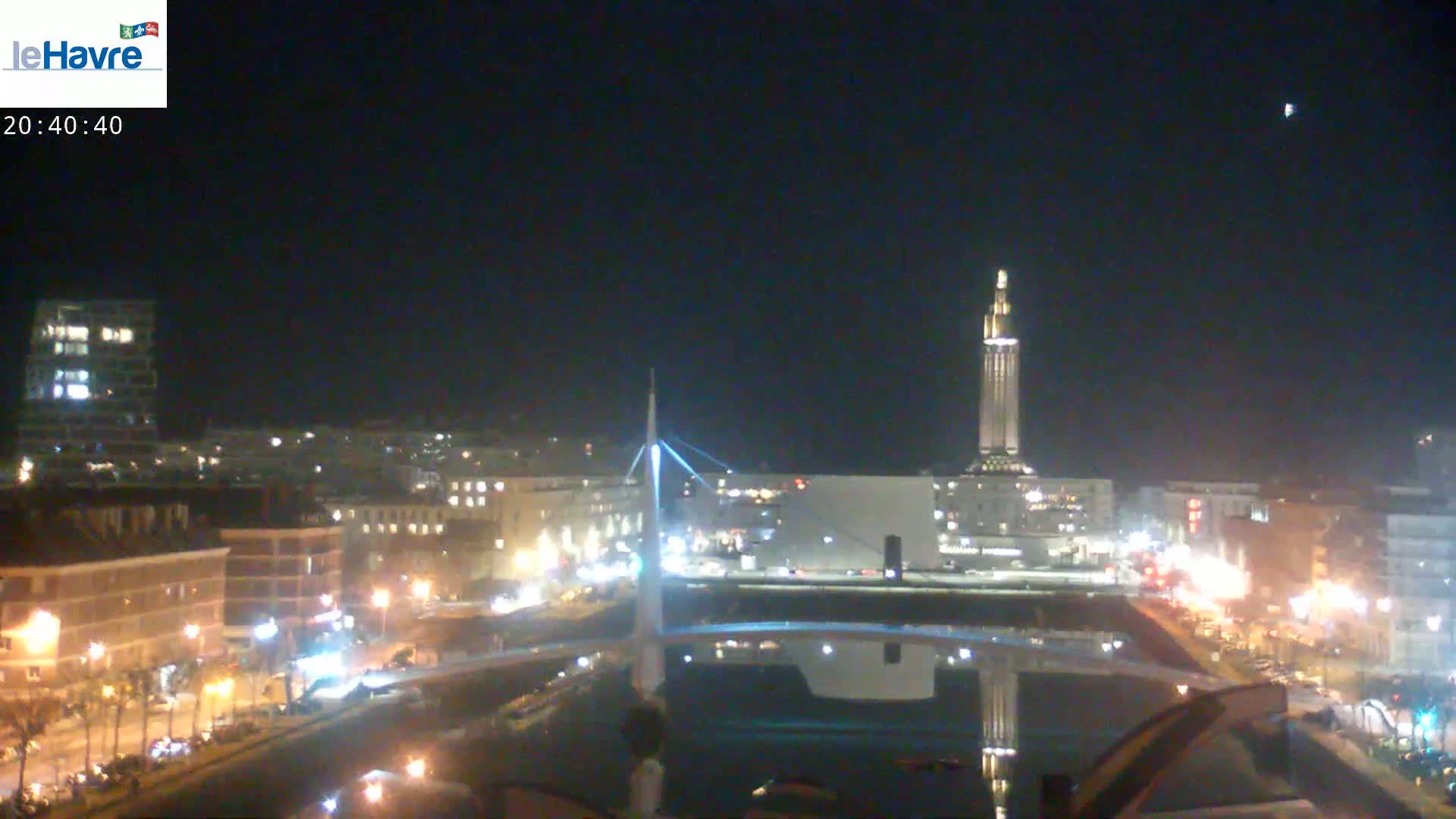A nighttime cityscape featuring a tall, slender tower, a bridge, and city streets illuminated with lights.