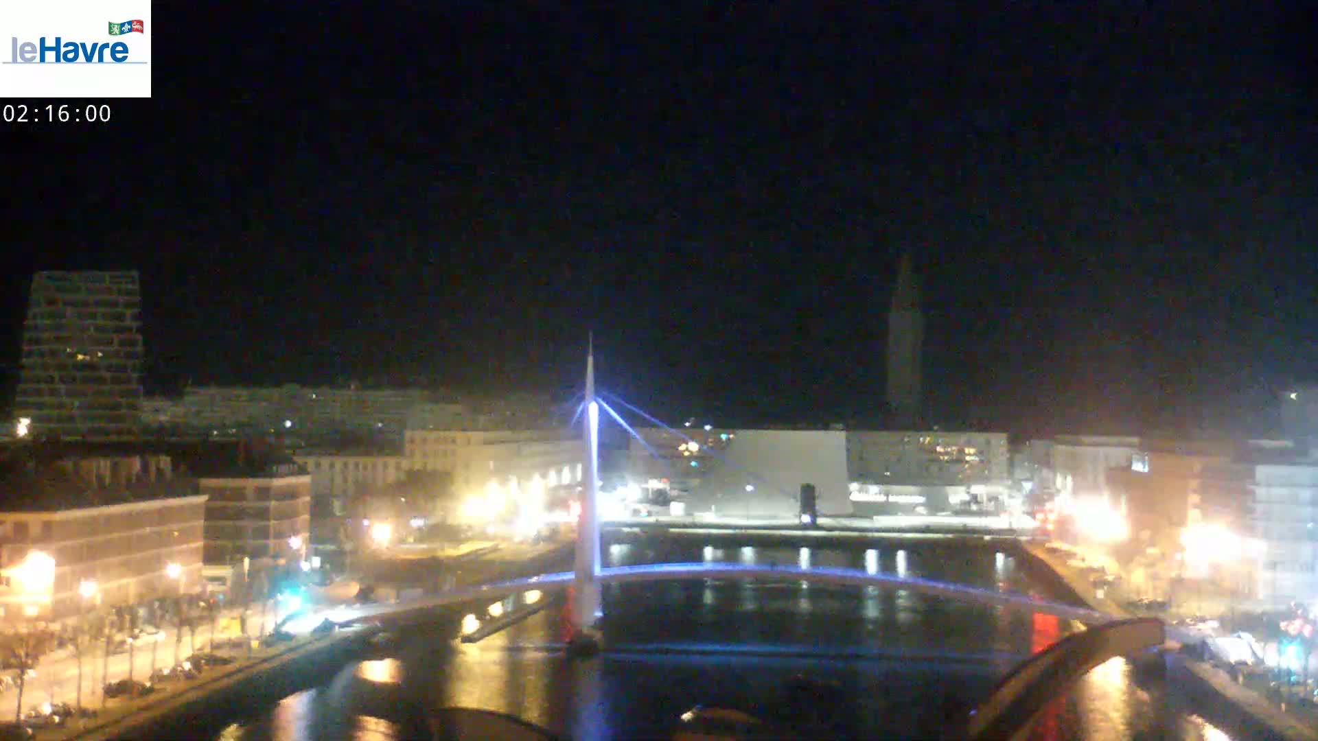 A nighttime view of a city with a lit-up bridge spanning a waterway, under a clear, dark sky.