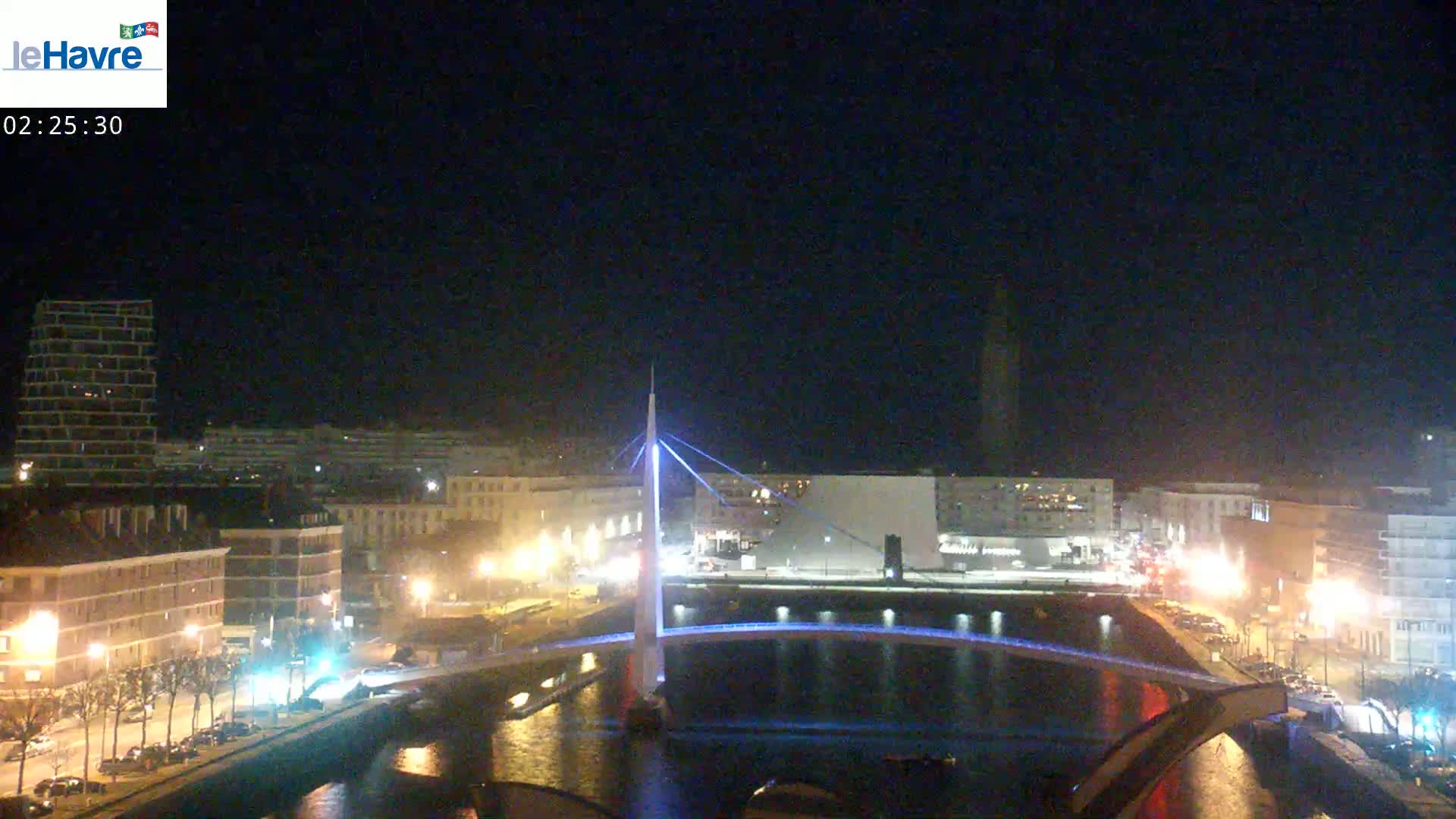A nighttime view of a city with a lit-up bridge spanning a waterway, under a clear, dark sky.