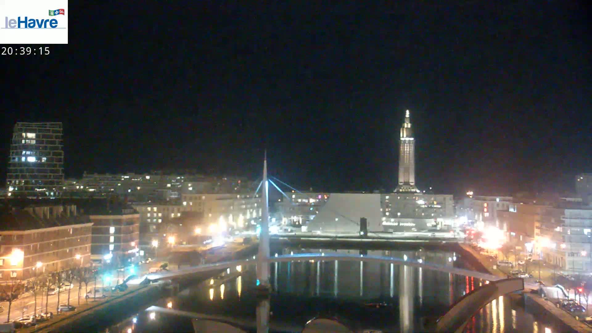 A nighttime cityscape with a river reflecting city lights, a tall tower, and a modern bridge.