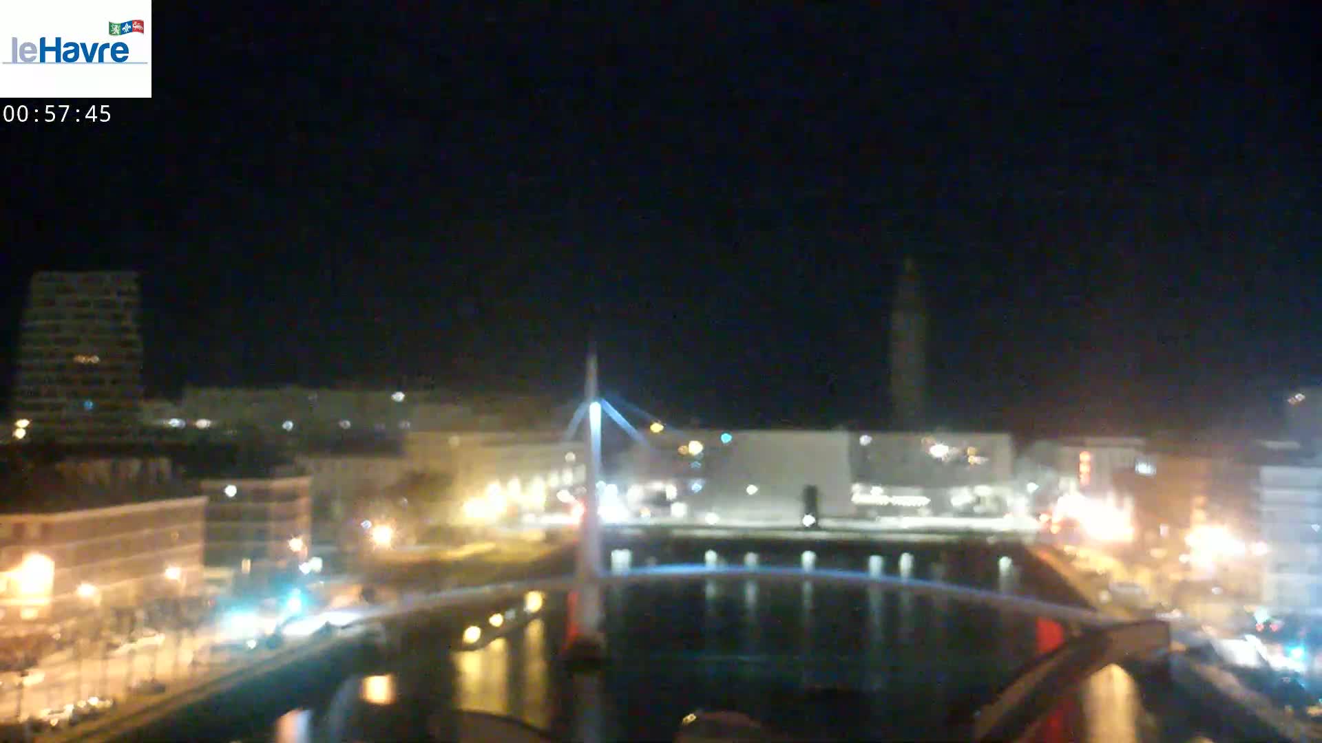 A nighttime cityscape featuring a bridge over a body of water, illuminated buildings, and streetlights.