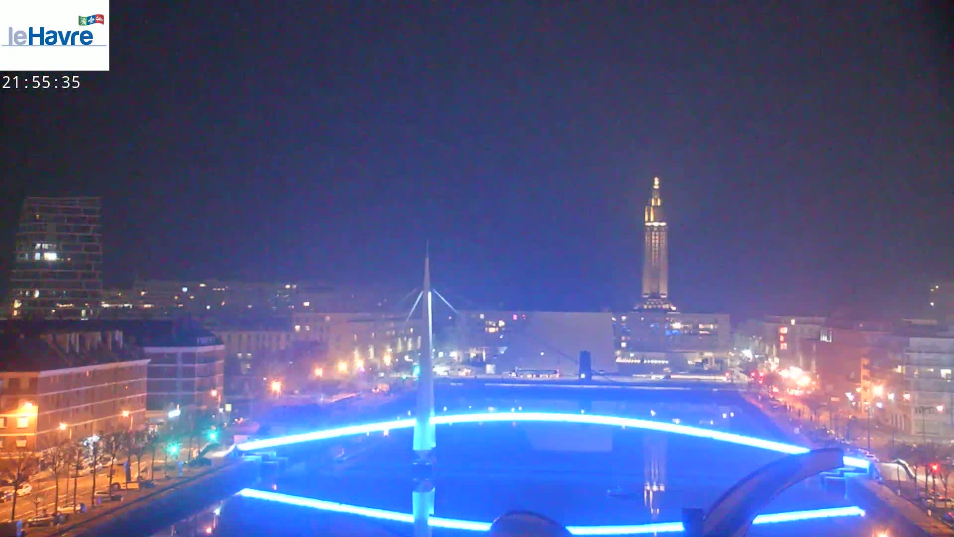 A nighttime cityscape with a tall tower in the background and a large, illuminated circular structure in the foreground.