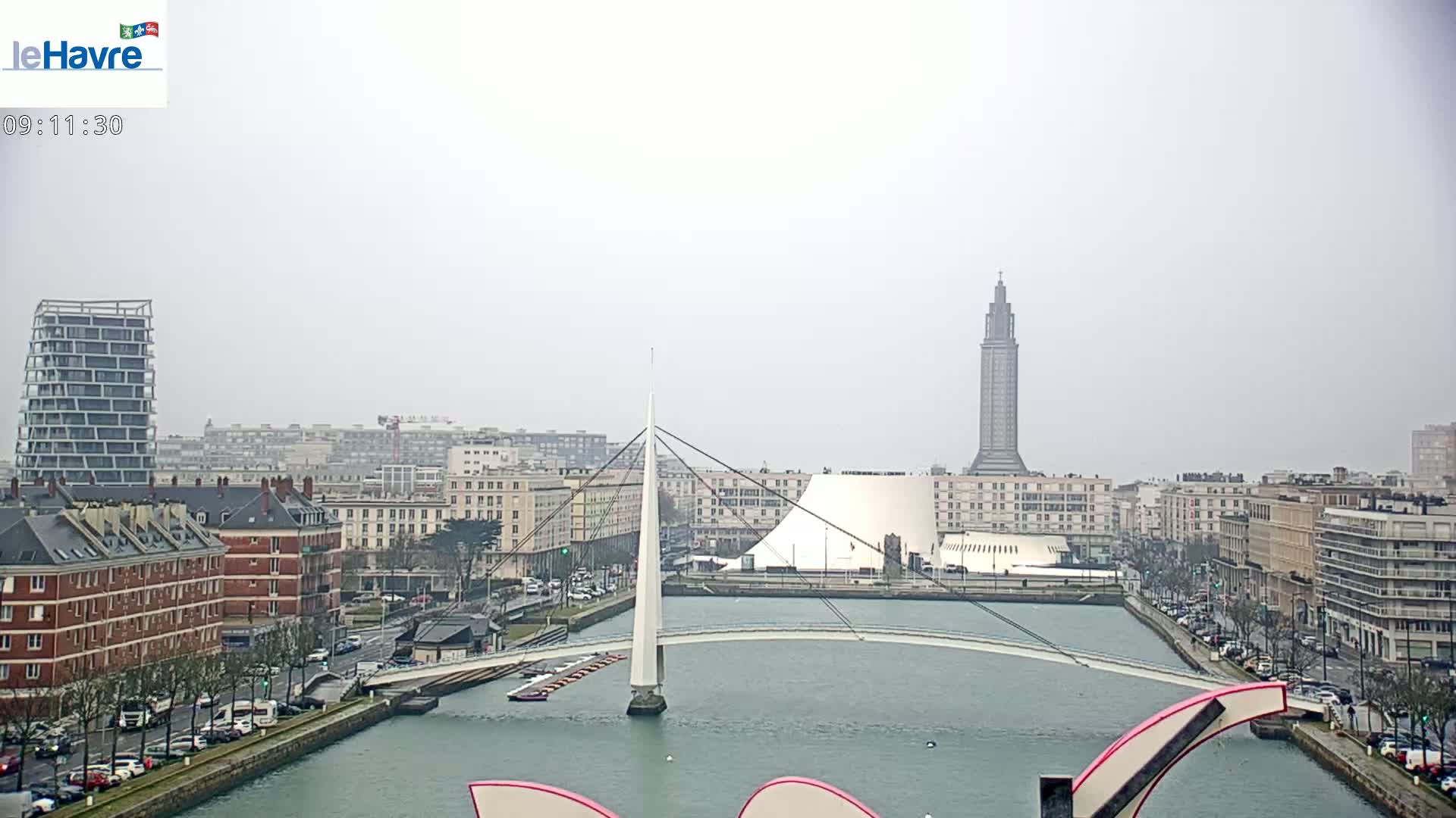 A city skyline with a white bridge spanning a canal, under an overcast sky.