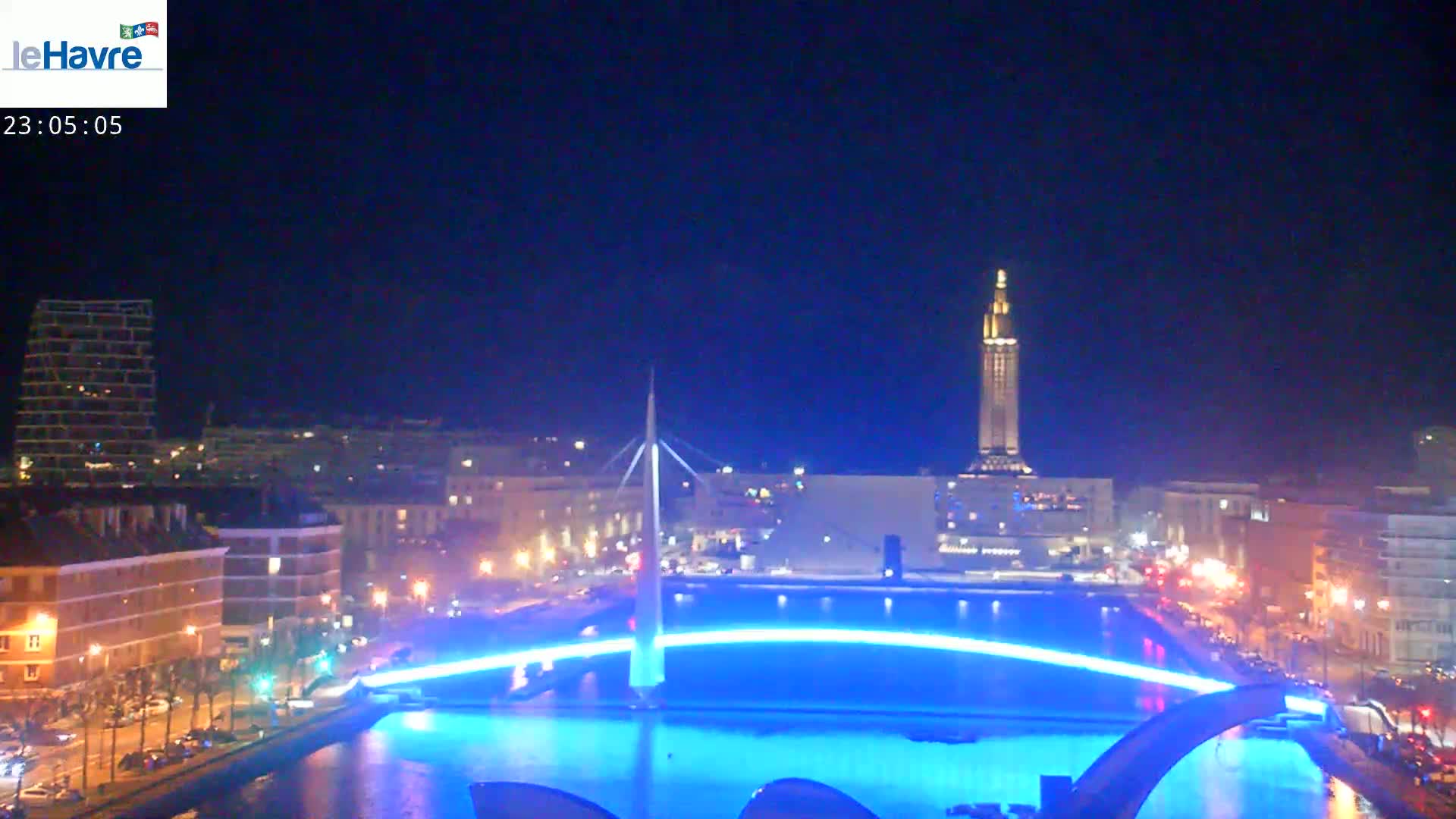 A nighttime cityscape with a lit-up bridge arching over a body of water, under a clear, dark sky.