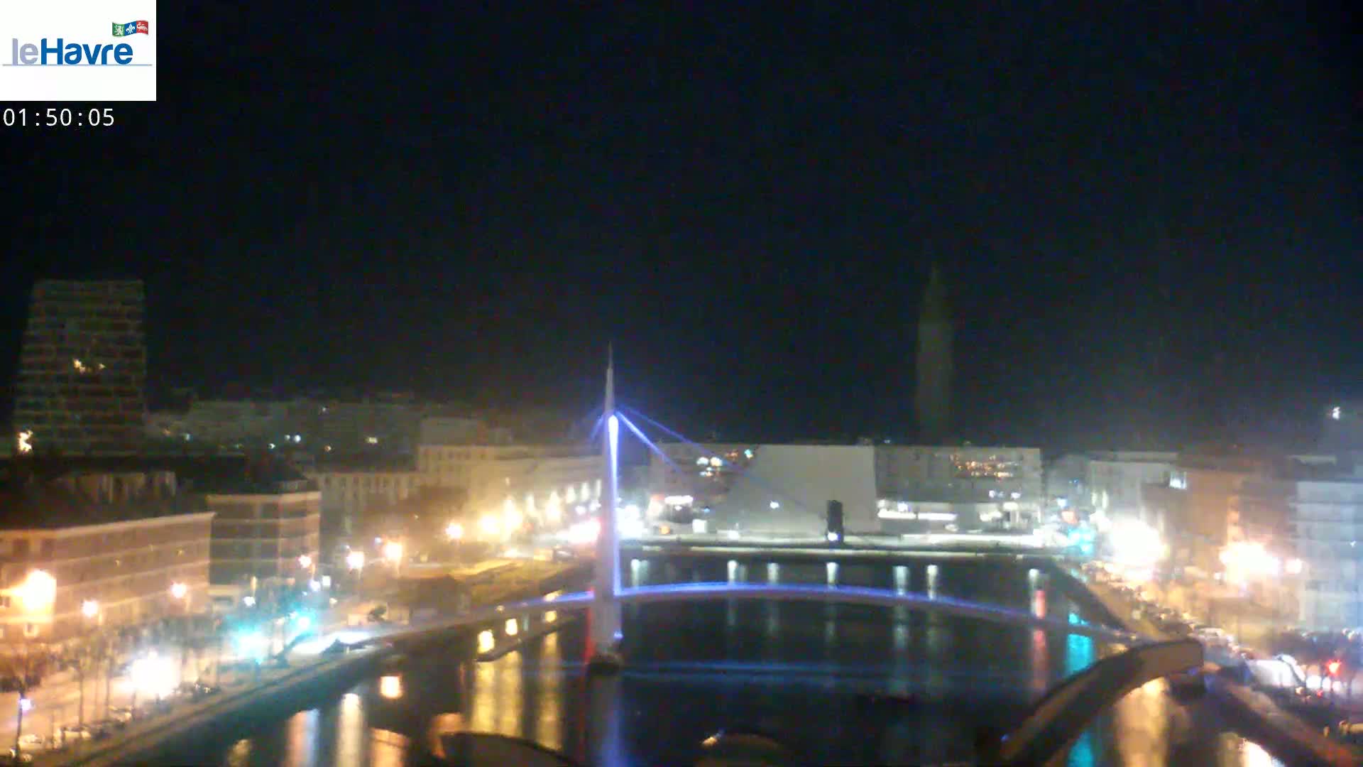 A nighttime cityscape showing a river with a lit bridge, buildings, and streetlights under a clear, dark sky.