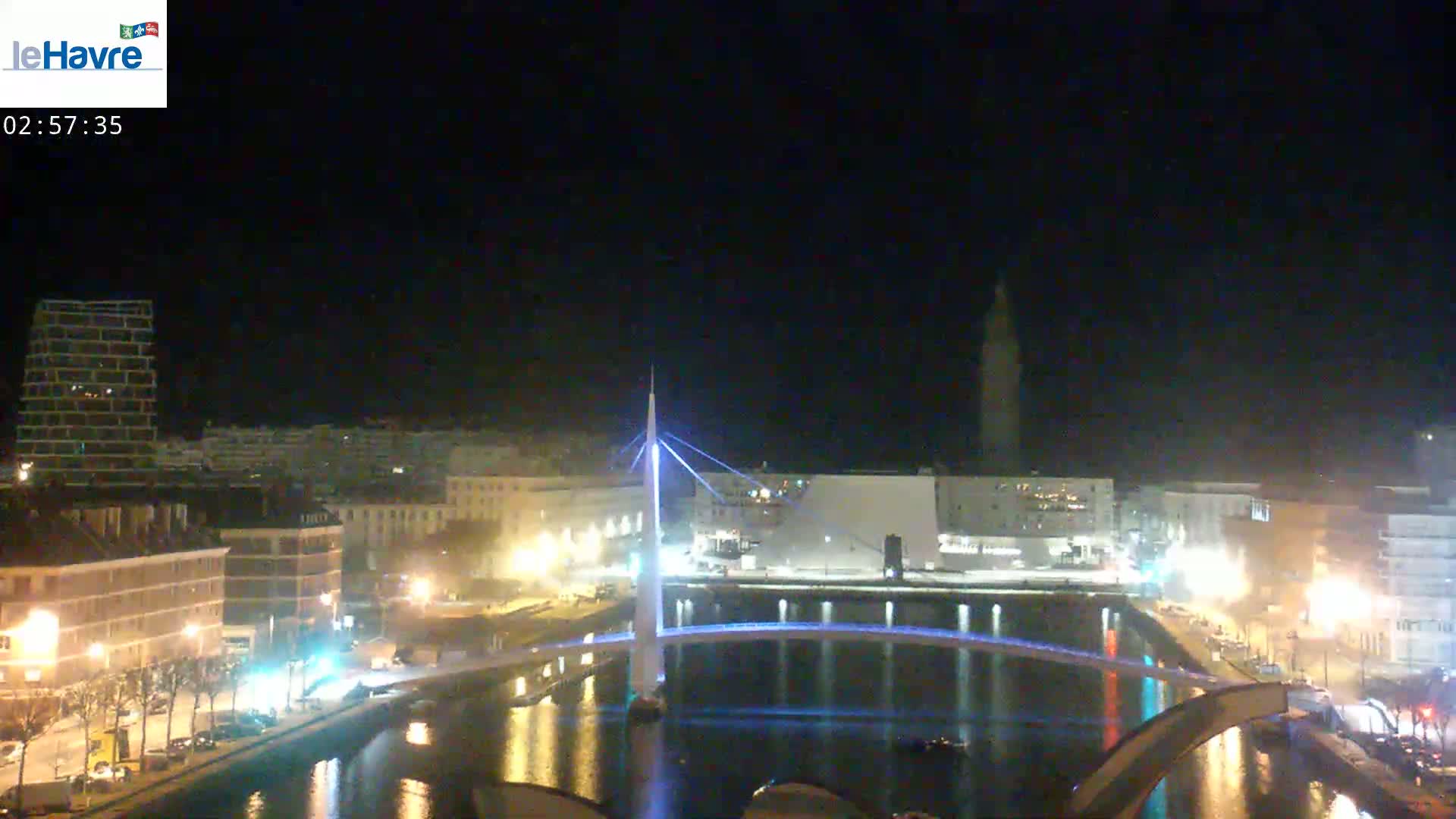 A nighttime view of a city with a lit-up bridge spanning a canal, surrounded by buildings and streetlights.