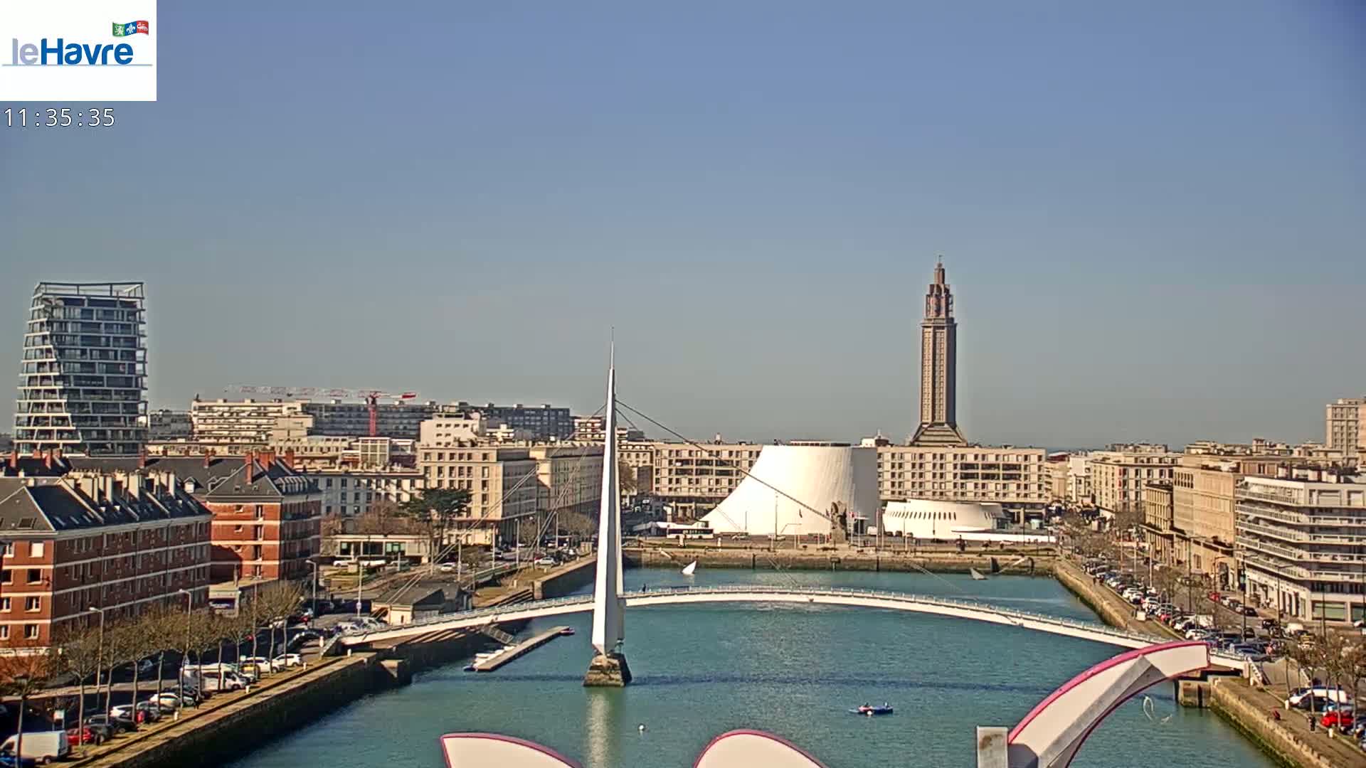 A city skyline with a modern white bridge crossing a waterway under a clear blue sky.