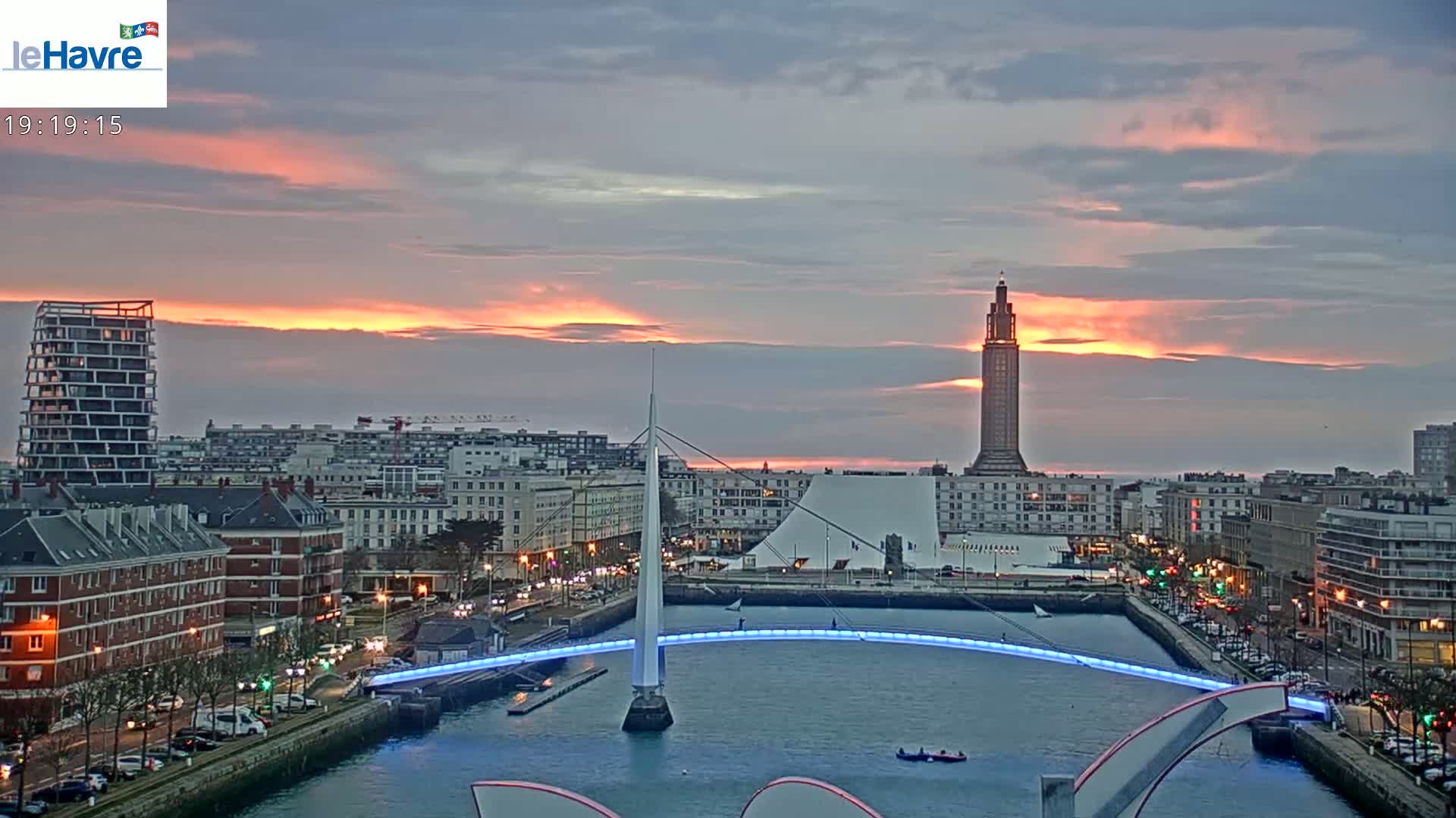 A city skyline with a modern bridge illuminated at sunset over a waterway.