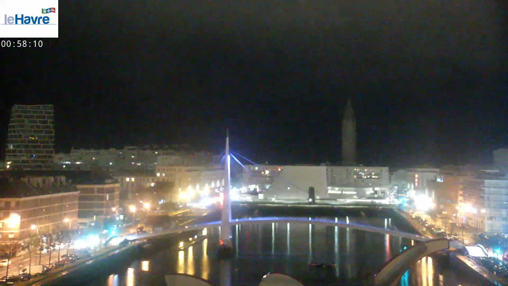 A nighttime view of a city harbor with a lit bridge, buildings, and calm water.