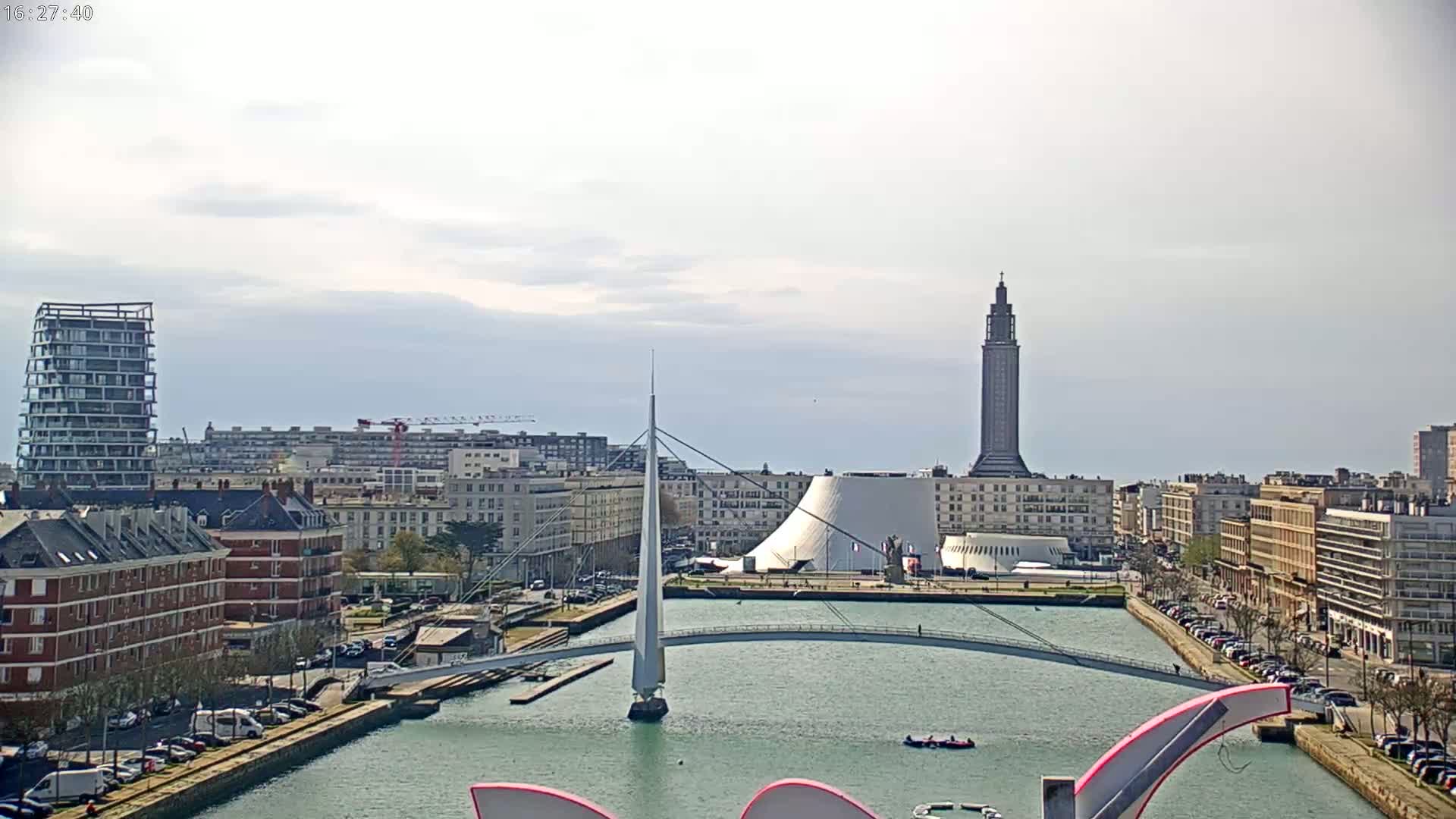 A cityscape with a canal, a modern bridge, and a tall tower under a partly cloudy sky.
