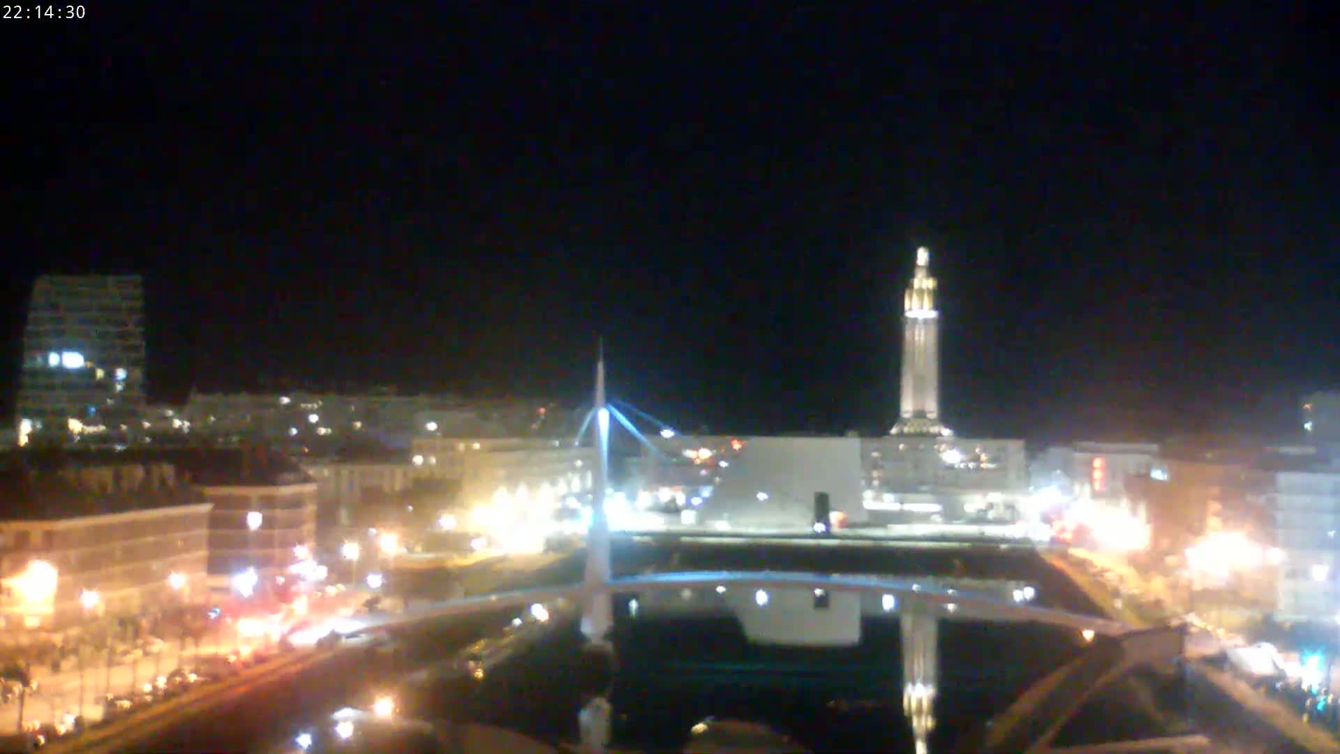 A nighttime view of a city with a bridge and tall tower illuminated, under a clear, dark sky.