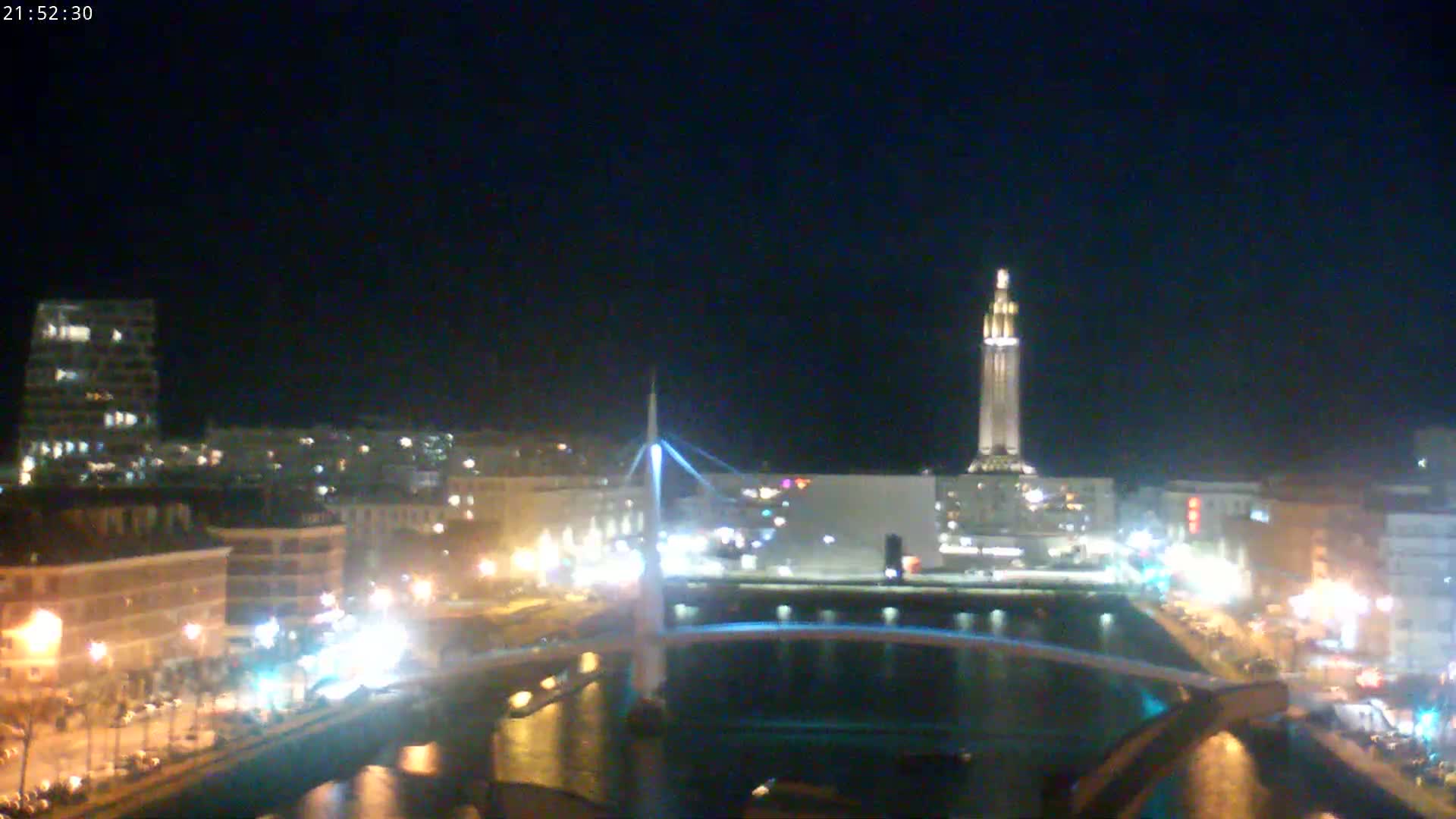 A nighttime view of a city with a lit-up tower and bridge over a waterway.