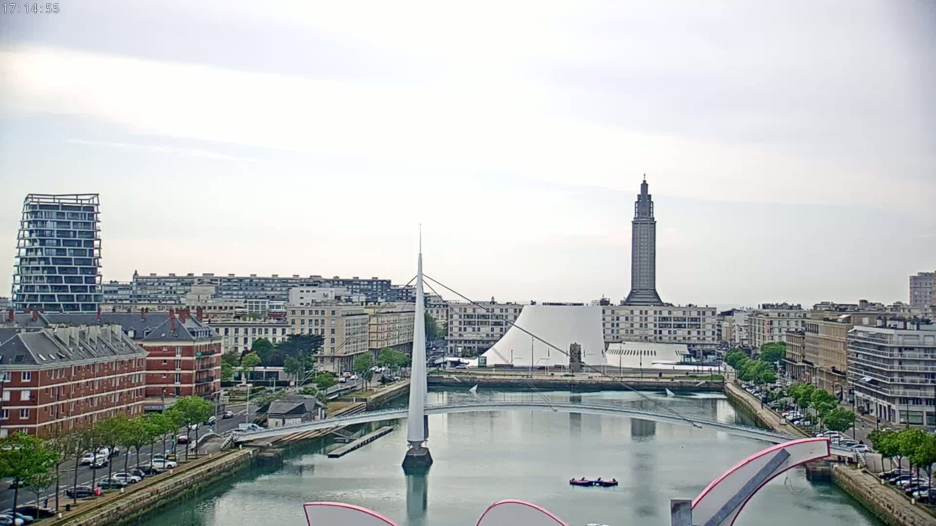 A city skyline with a modern white bridge spanning a calm waterway, under an overcast sky.