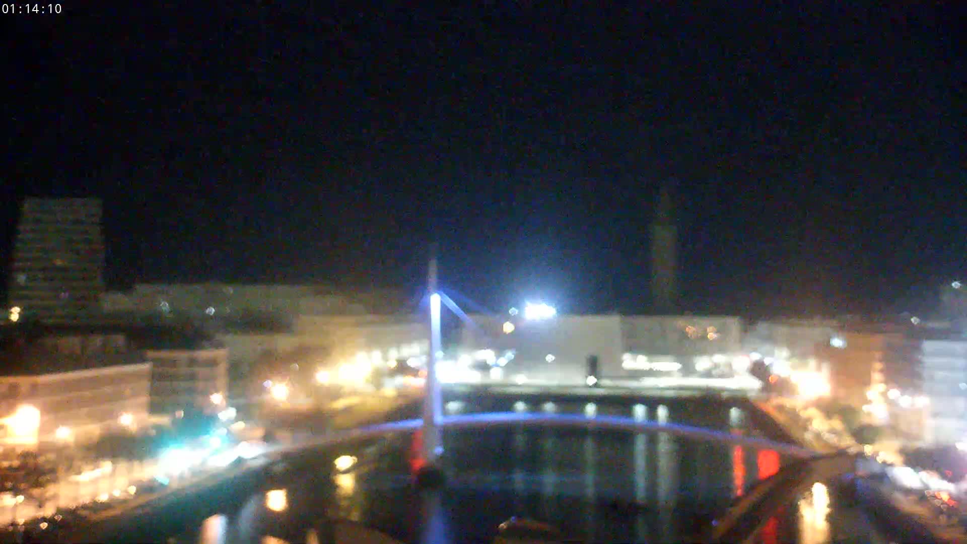A nighttime view of a city harbor with a lit bridge and buildings, under a clear dark sky.