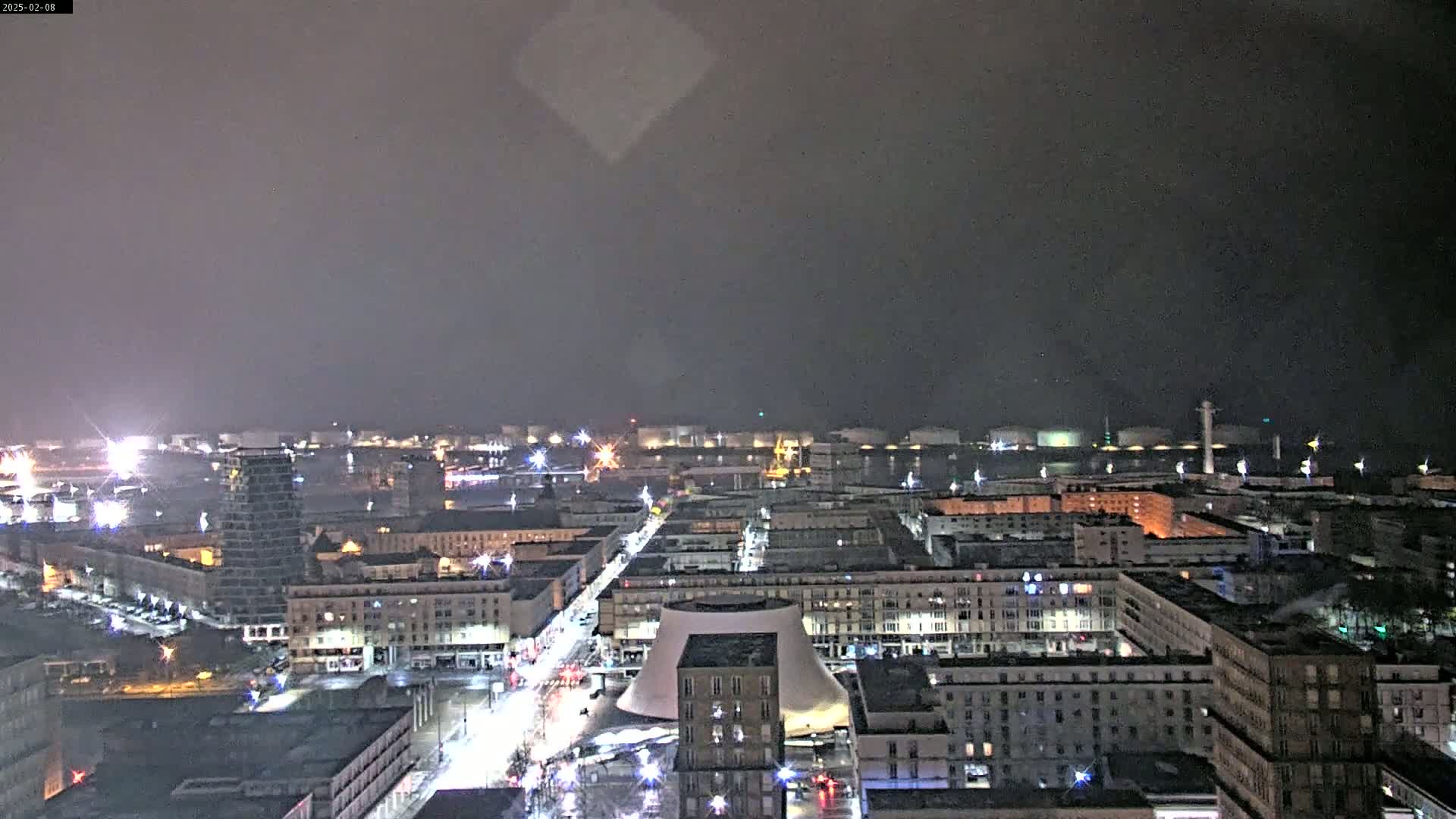 A nighttime view of a city illuminated with streetlights under a dark, overcast sky.